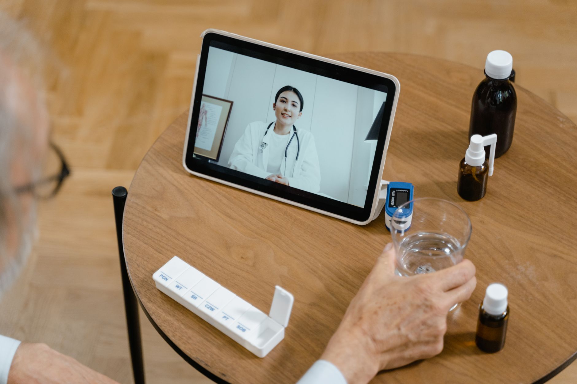 An elderly man at home participating in a virtual prehab session with a physiotherapist on a tablet.
