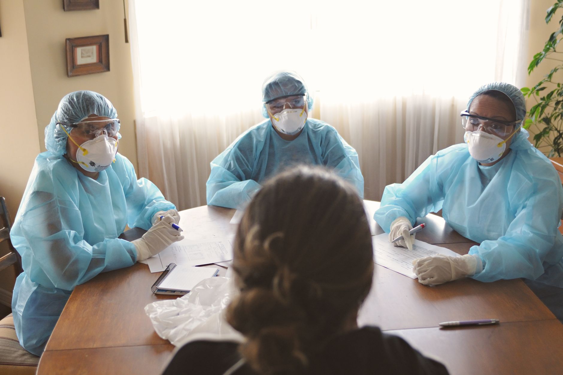 Three infection control specialists in PPE discuss data at a table.