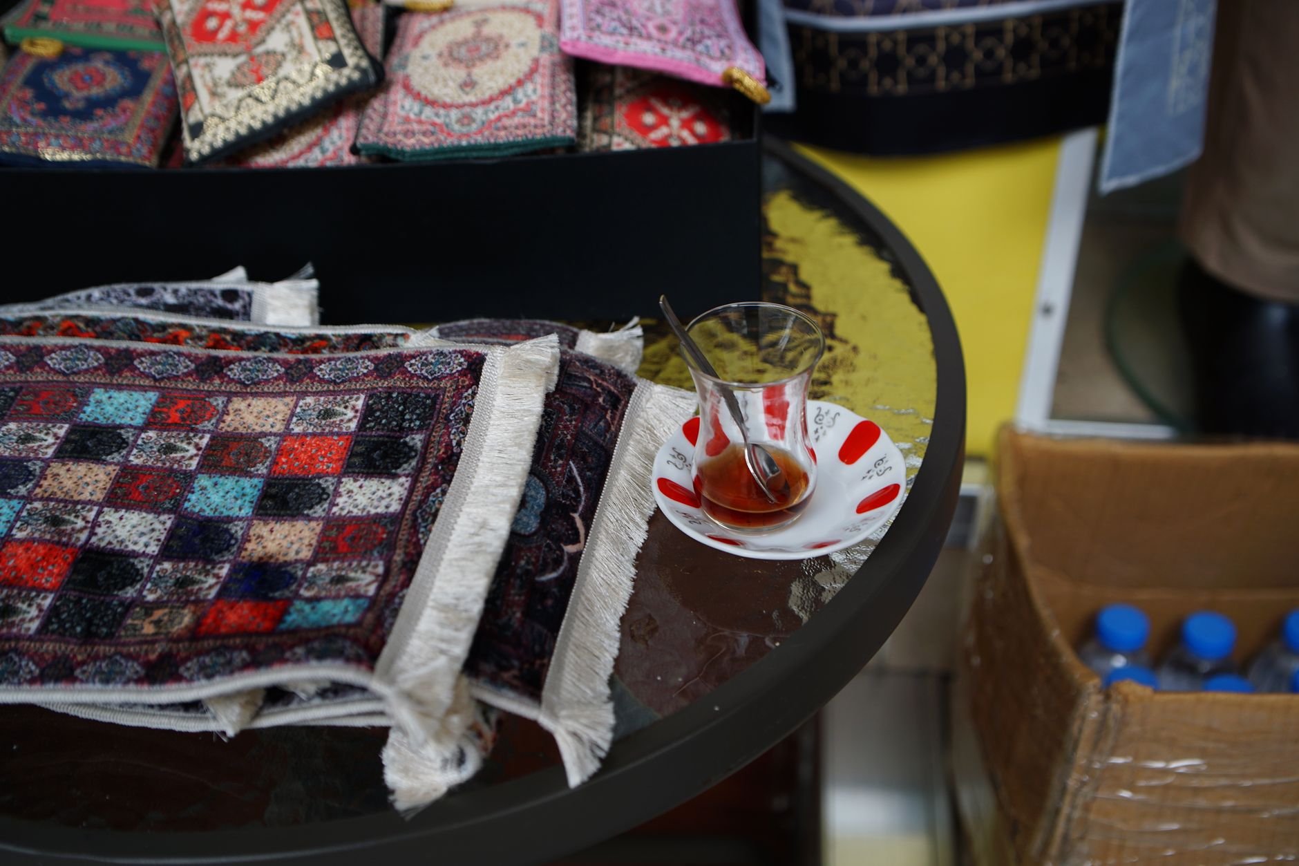 Glass of tea on a decorative plate beside colorful textiles in a shop.
