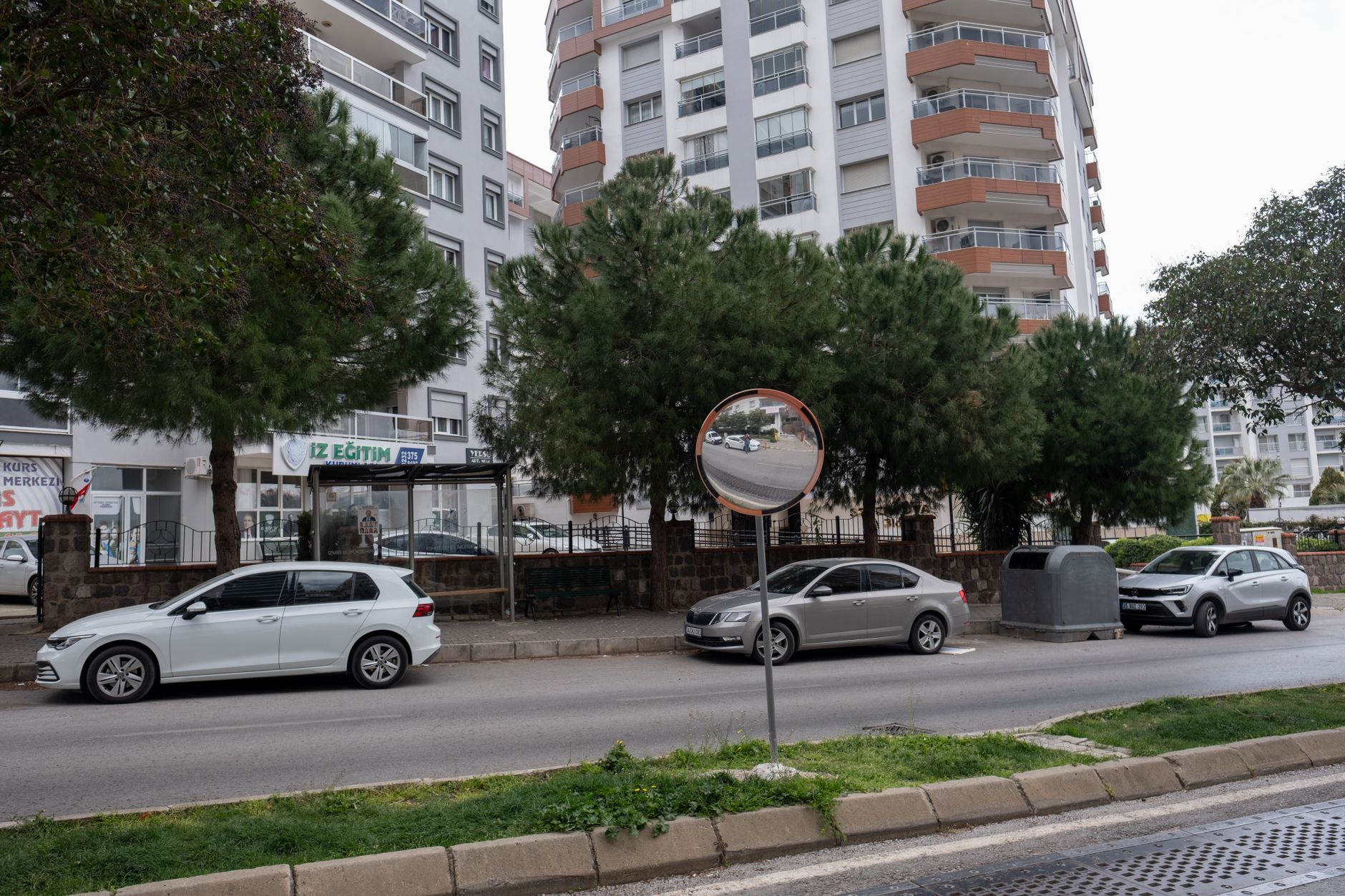View of a street in Turkey featuring parked cars, trees, and a reflective safety mirror.