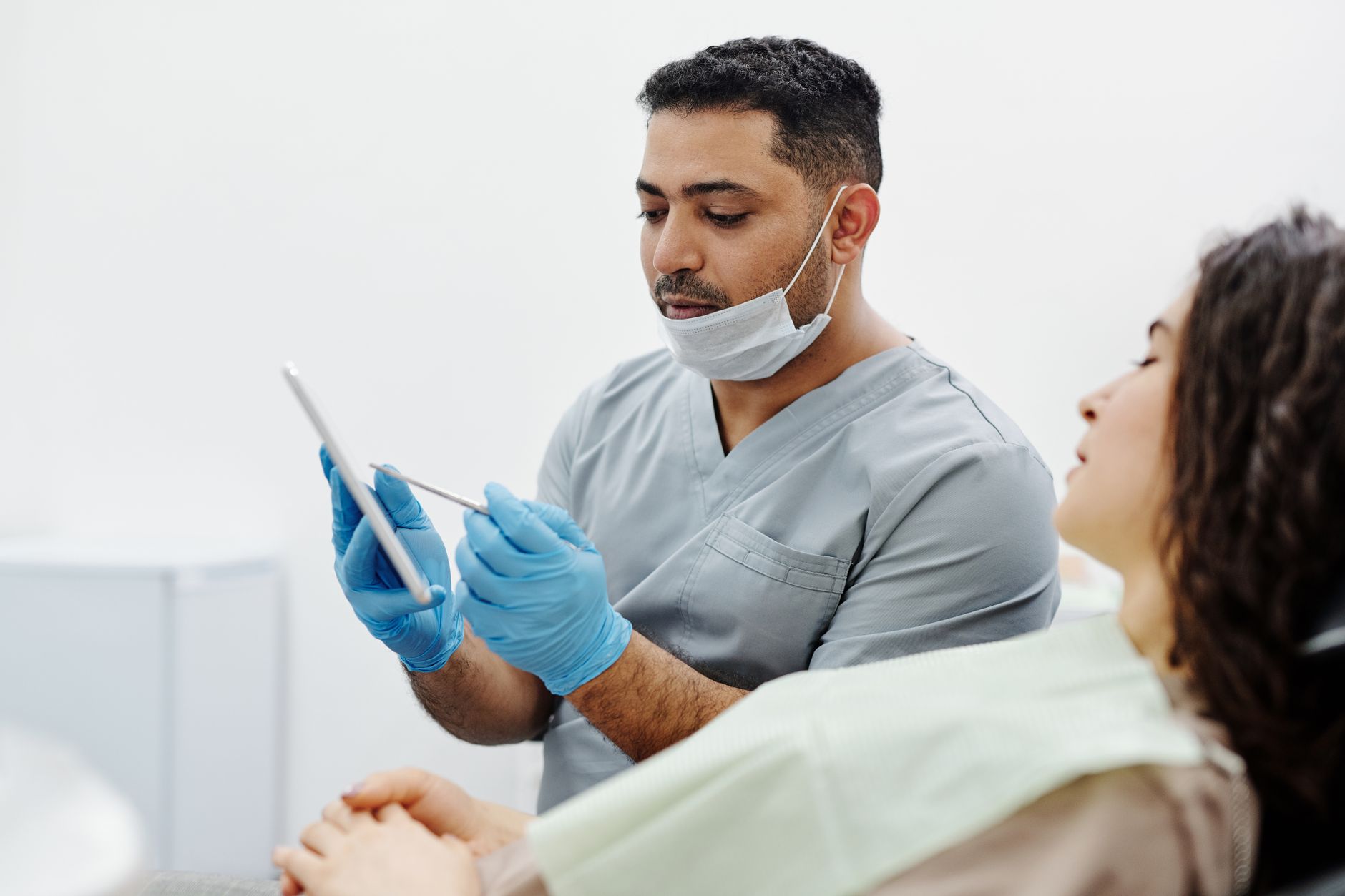 A Turkish doctor in scrubs studies patient records on a tablet in a dental clinic.