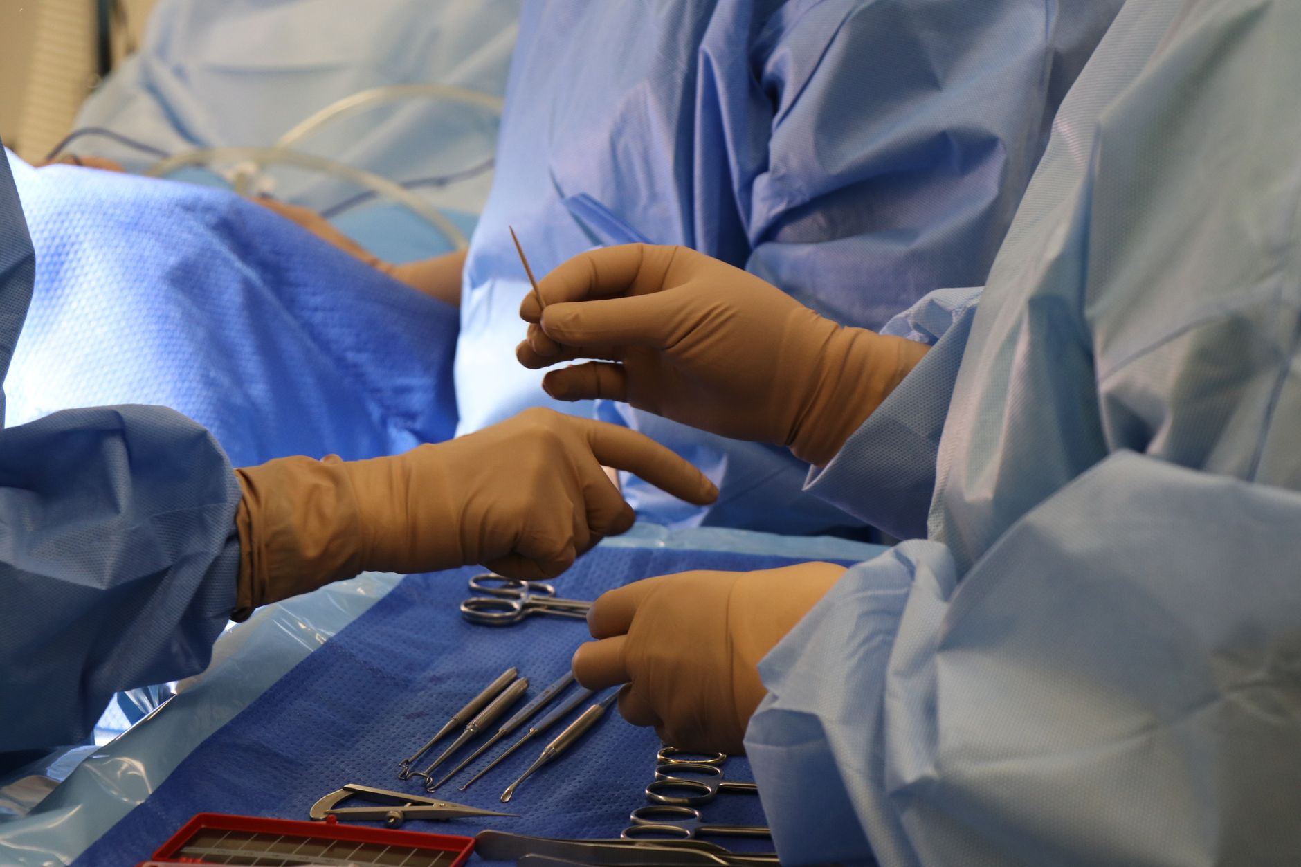 Hands of medical professionals in blue gowns performing a thrombectomy procedure in an angiography suite.