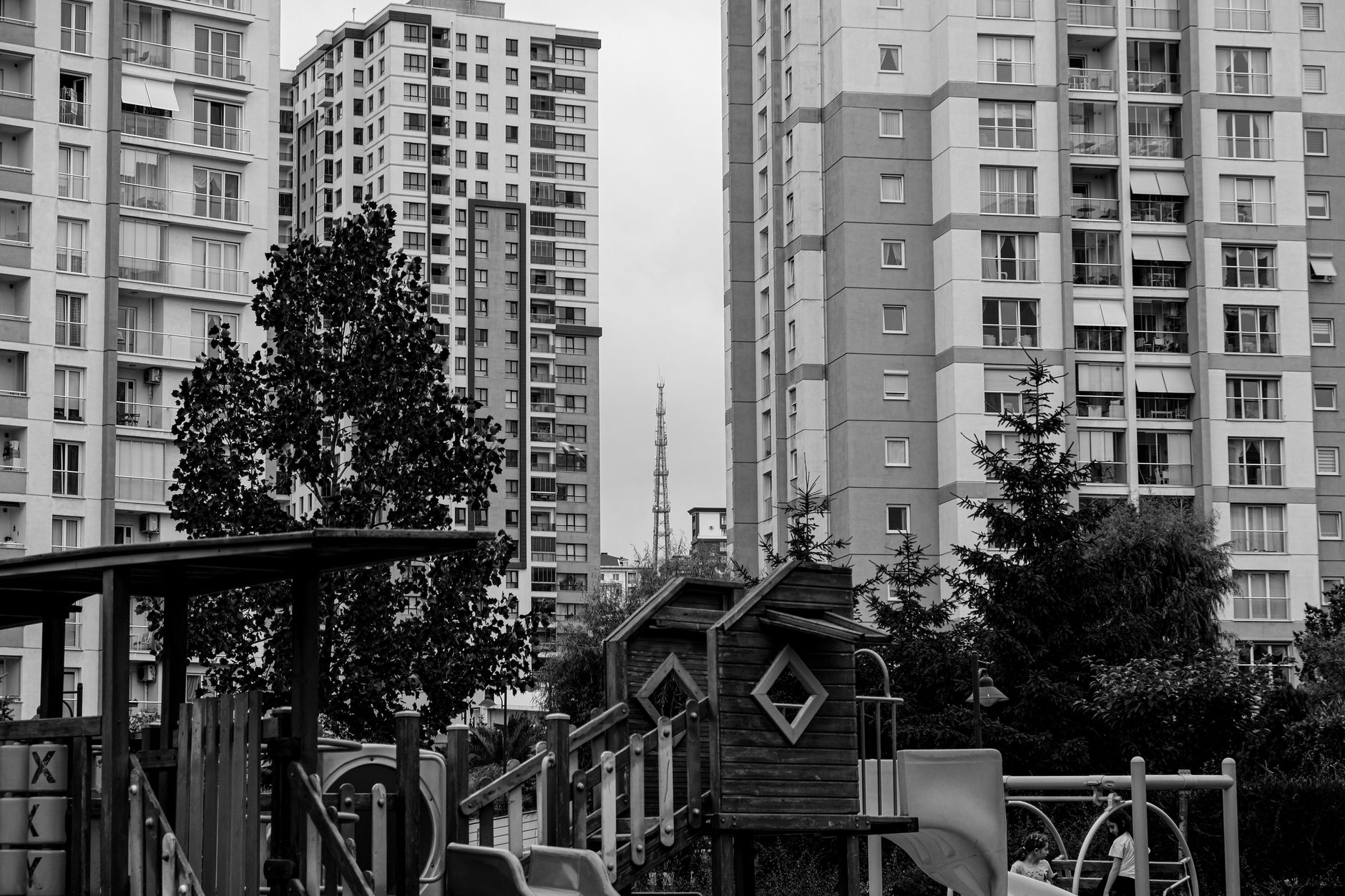 A children's play area surrounded by tall buildings in a Turkish hospital, featuring play structures and trees.