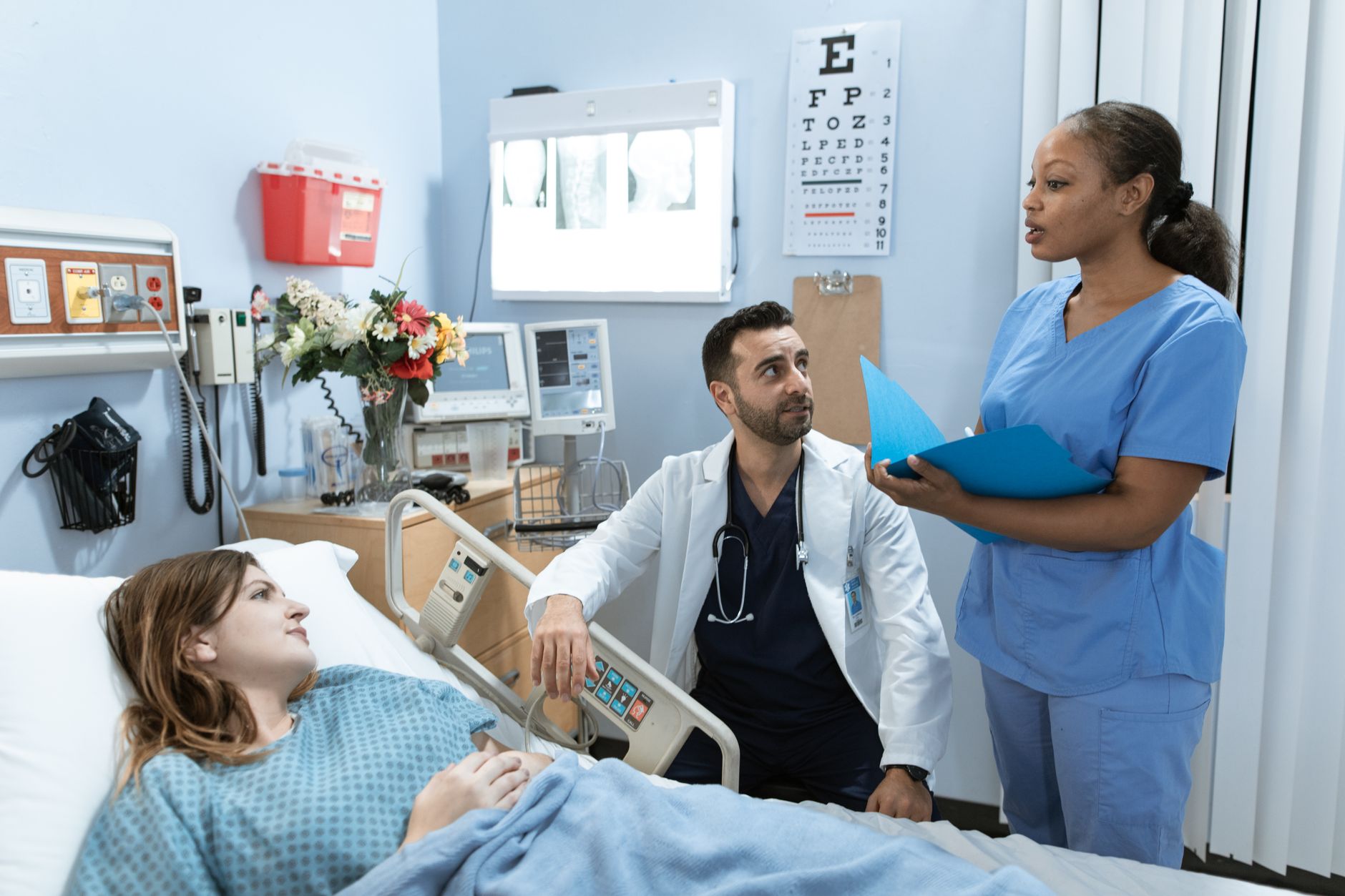 A nurse discussing a care plan with a doctor and a patient in a hospital room.