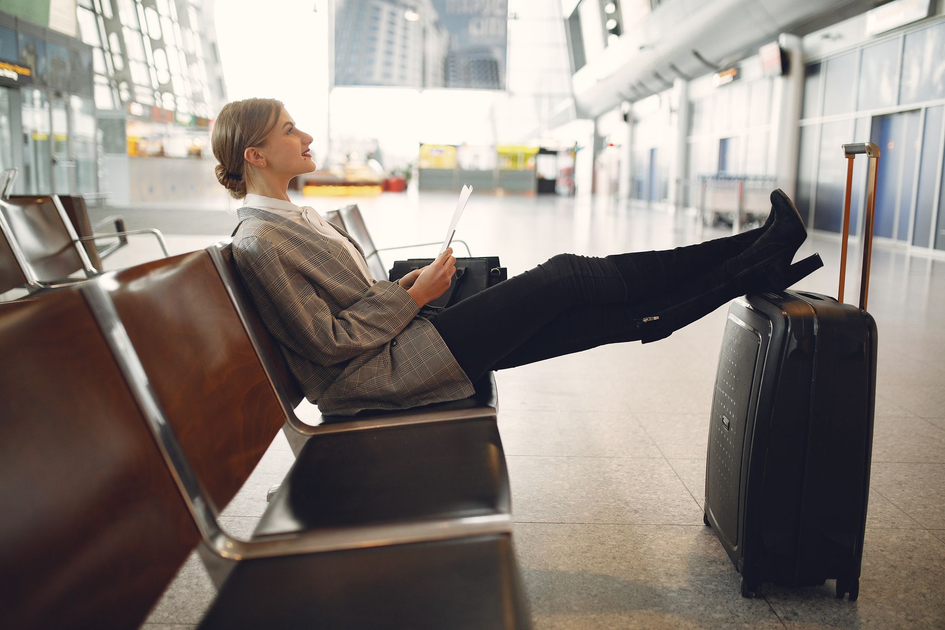 A patient in an airport wearing compression stockings, sitting with feet on luggage, reviewing documents.