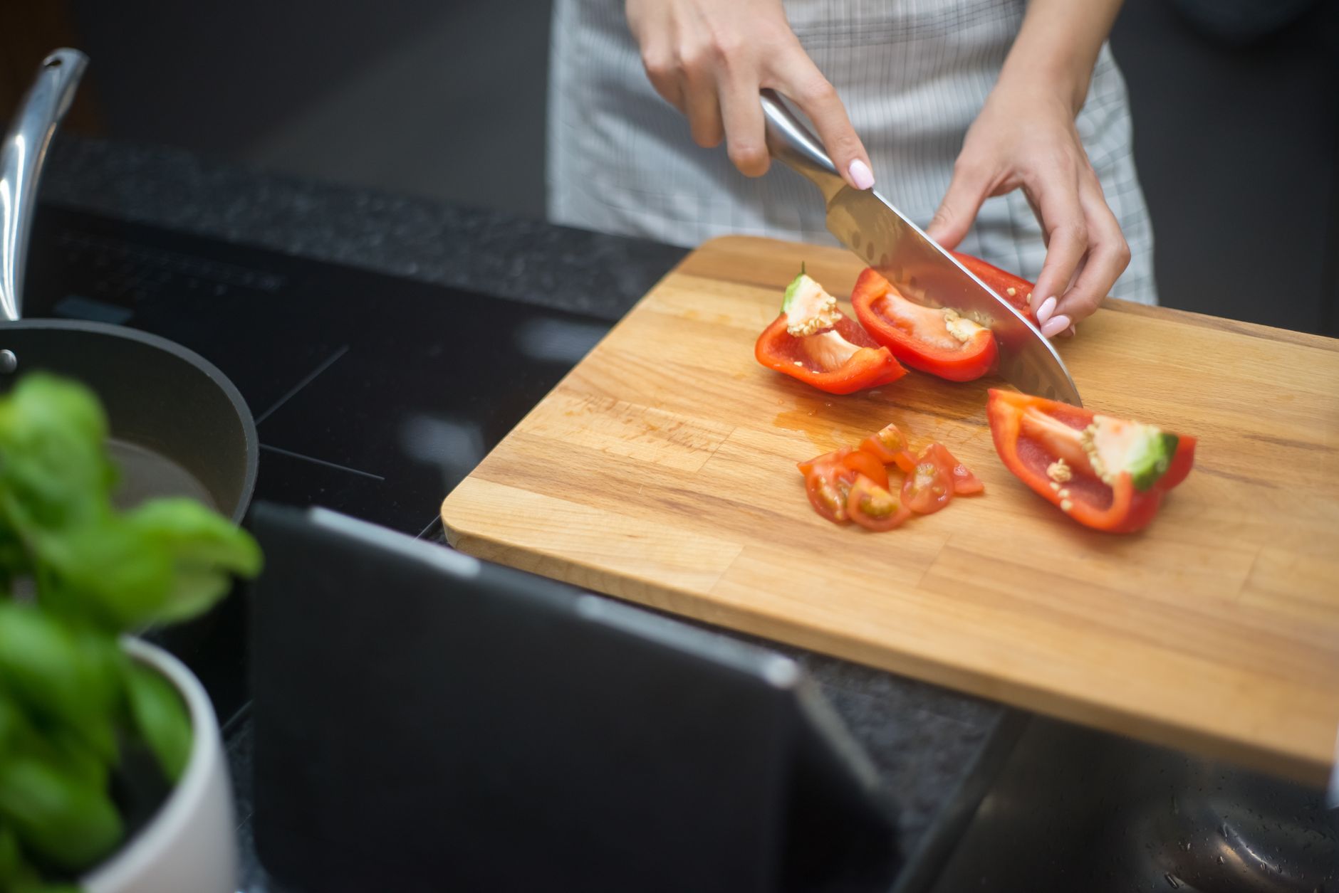 A person slicing red bell peppers on a wooden cutting board in a kitchen.