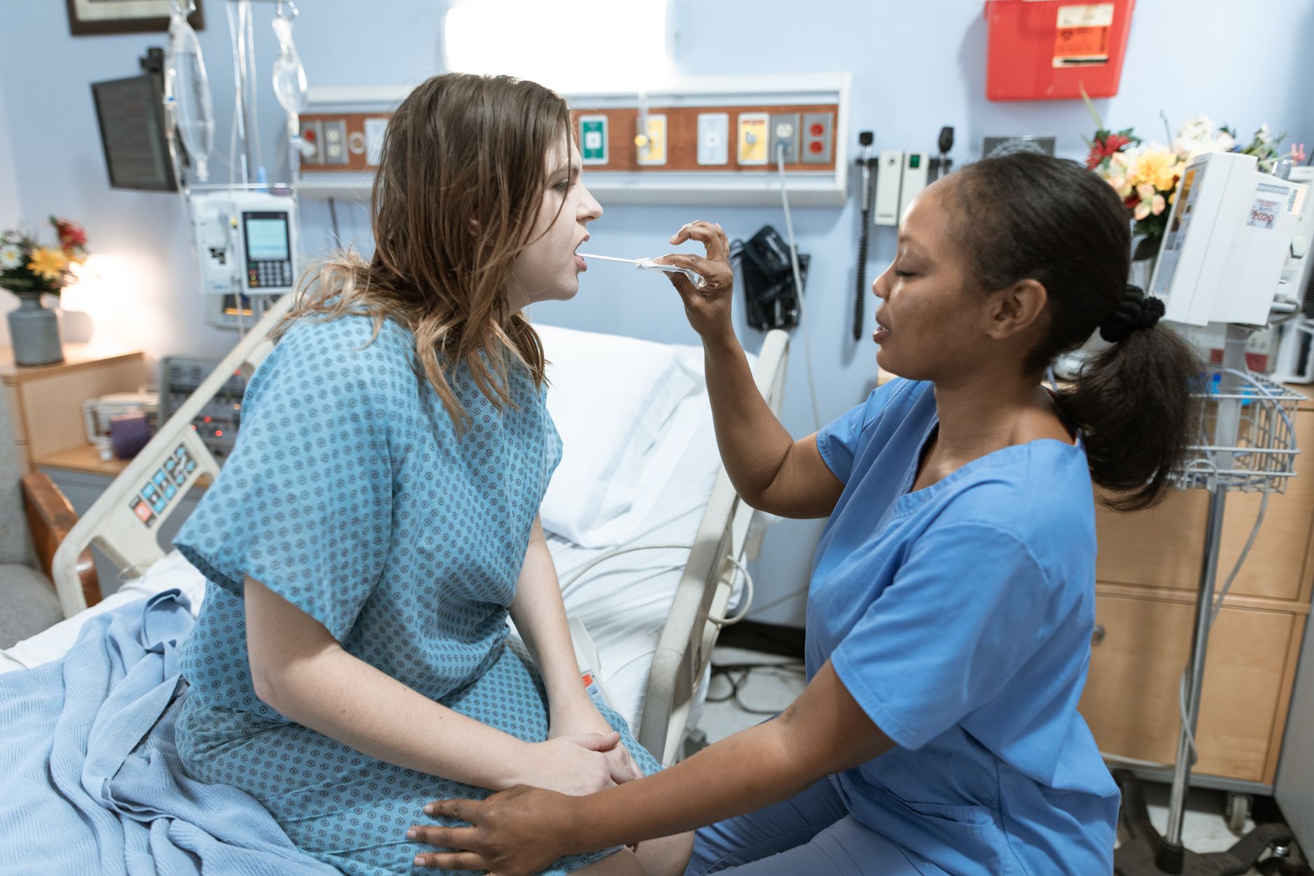 A nurse checks a patient's throat in a hospital recovery suite.