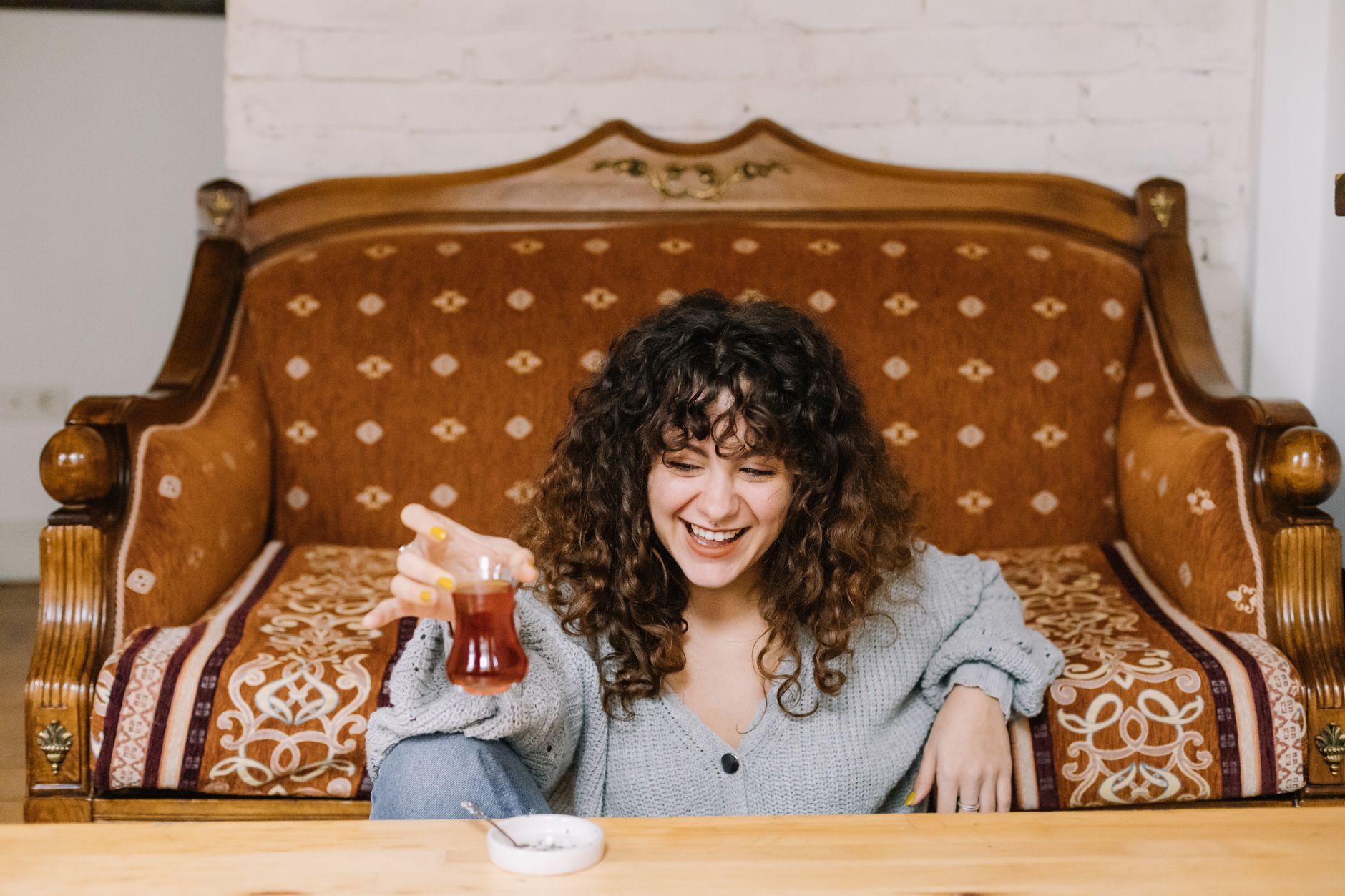 Smiling woman with curly hair holding a tea glass, relaxing at home.