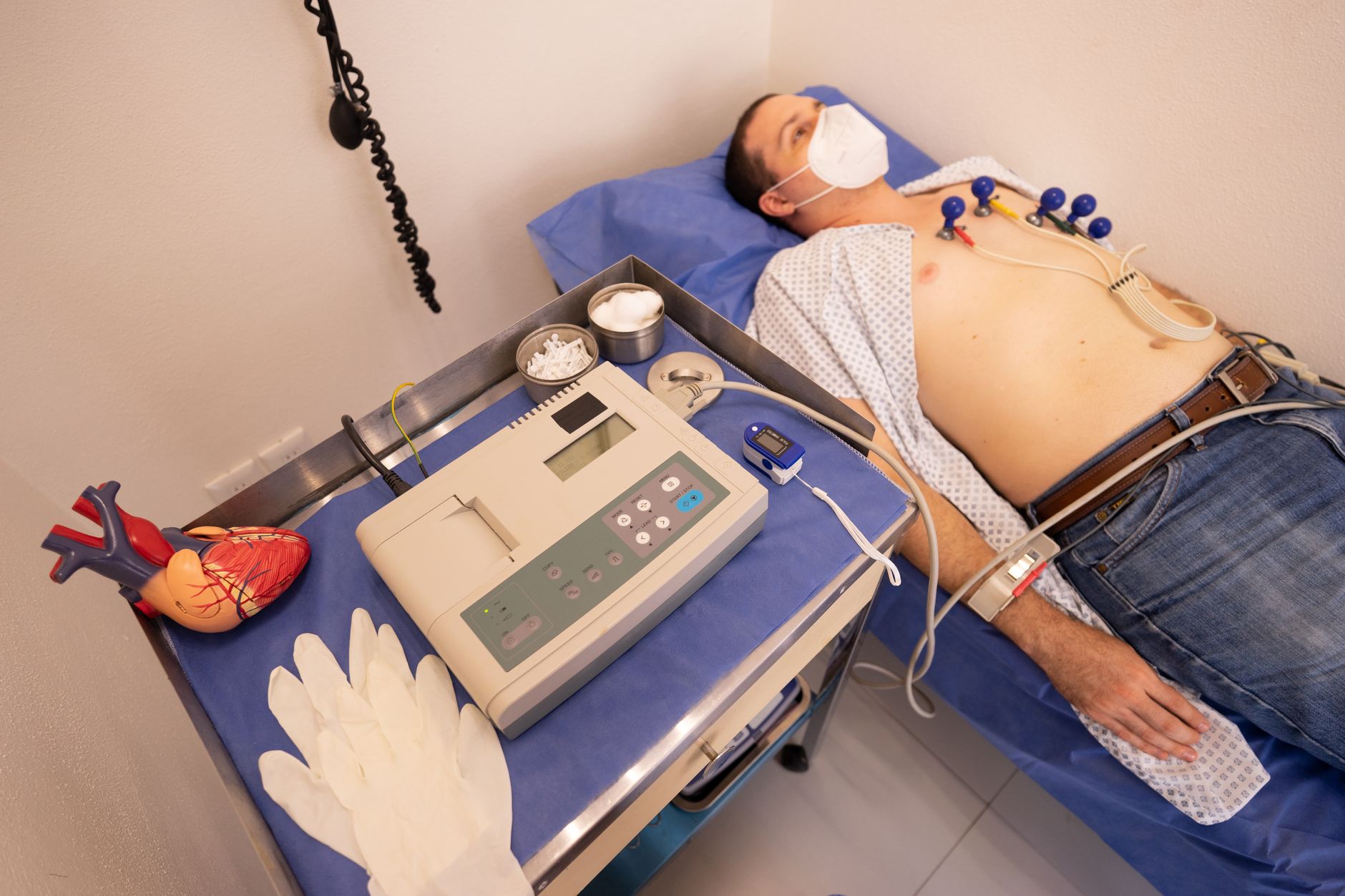 A patient in a clinical setting receiving an ECG test with electrodes attached and a monitor nearby.