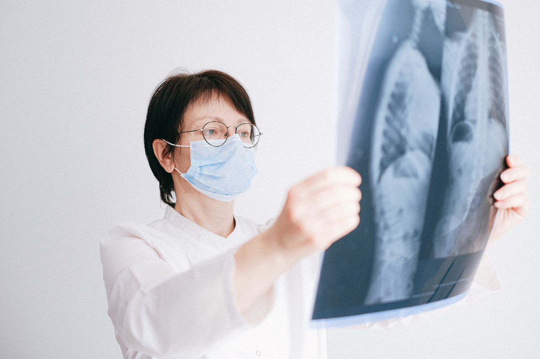 Technician in a mask holding an X-ray of lungs, evaluating the image.