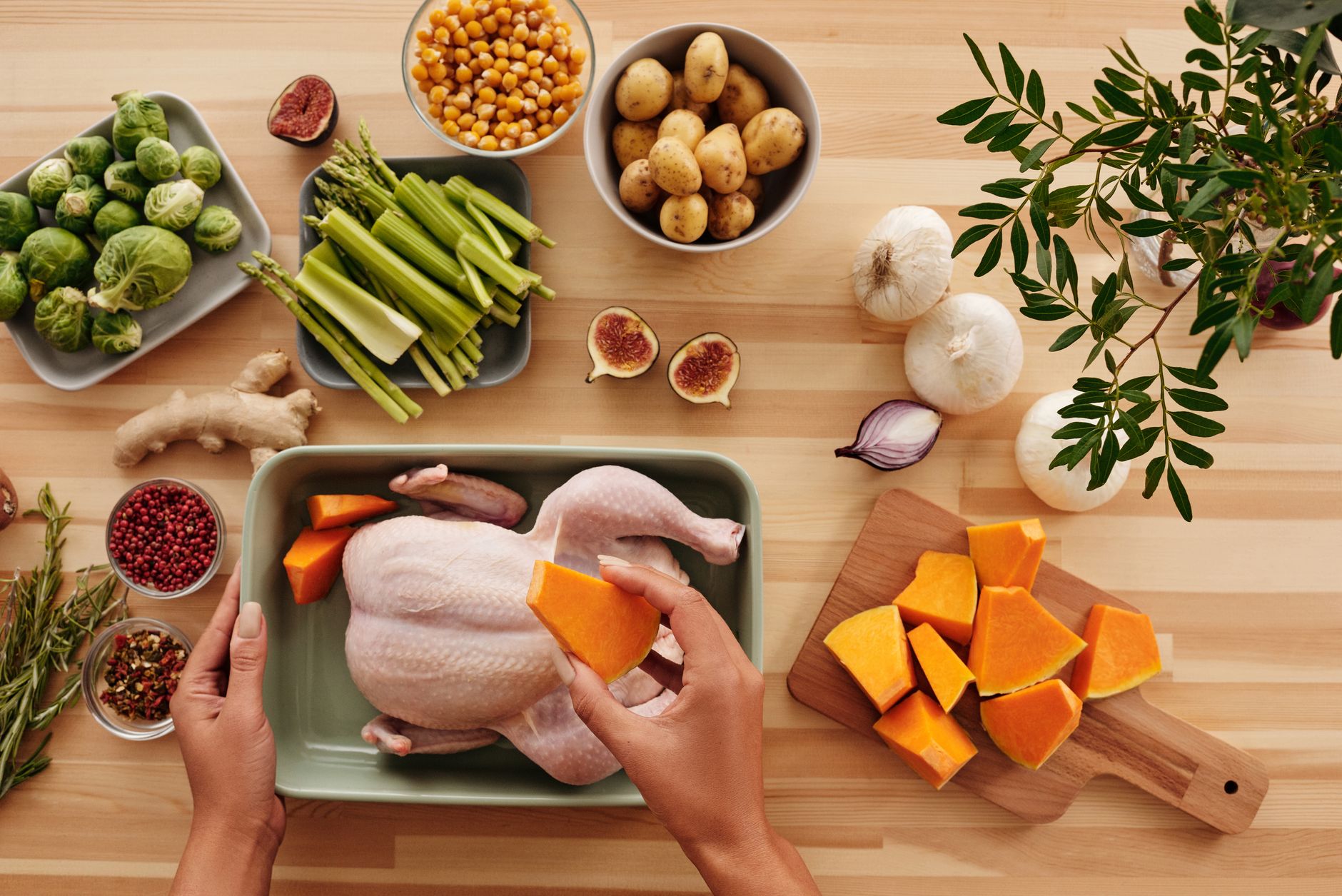 Hands preparing a chicken with butternut squash and fresh vegetables for a nutritious meal.