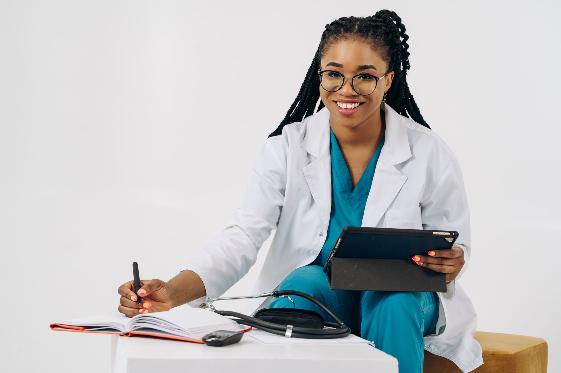A doctor in a white coat reviews digital records on a tablet, taking notes in a hospital setting.