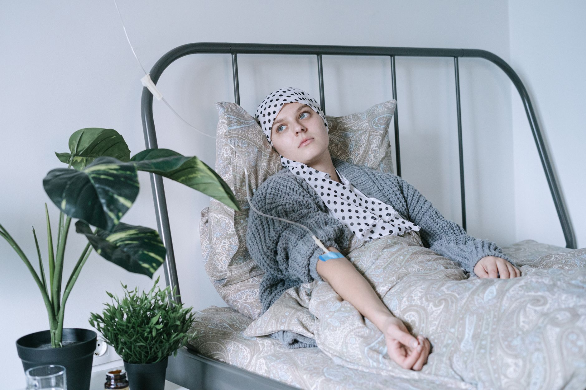 Young patient in a bed with an IV, wearing a polka dot scarf, in a tranquil room with plants.