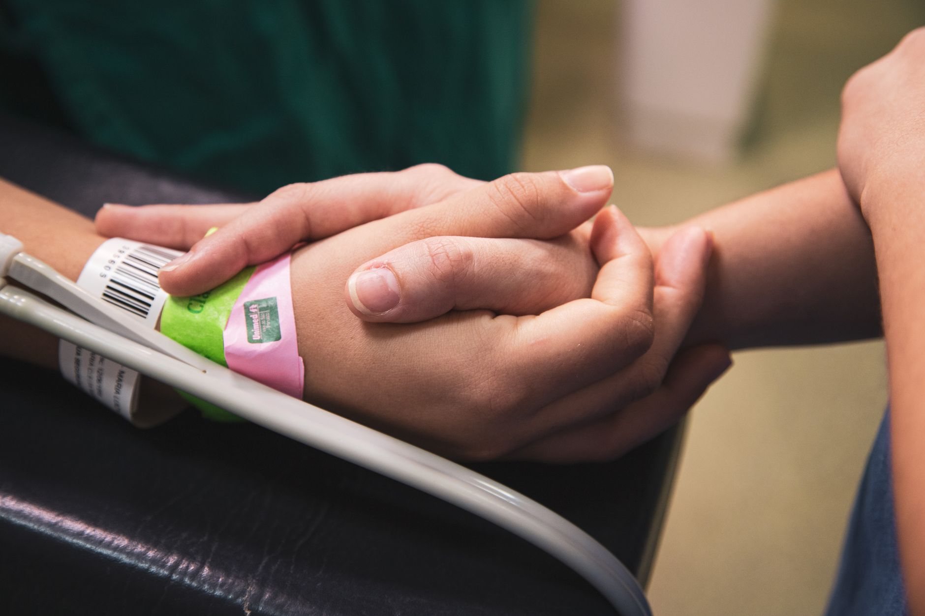 Close-up of patient wristband in hospital, with two hands holding each other for support.