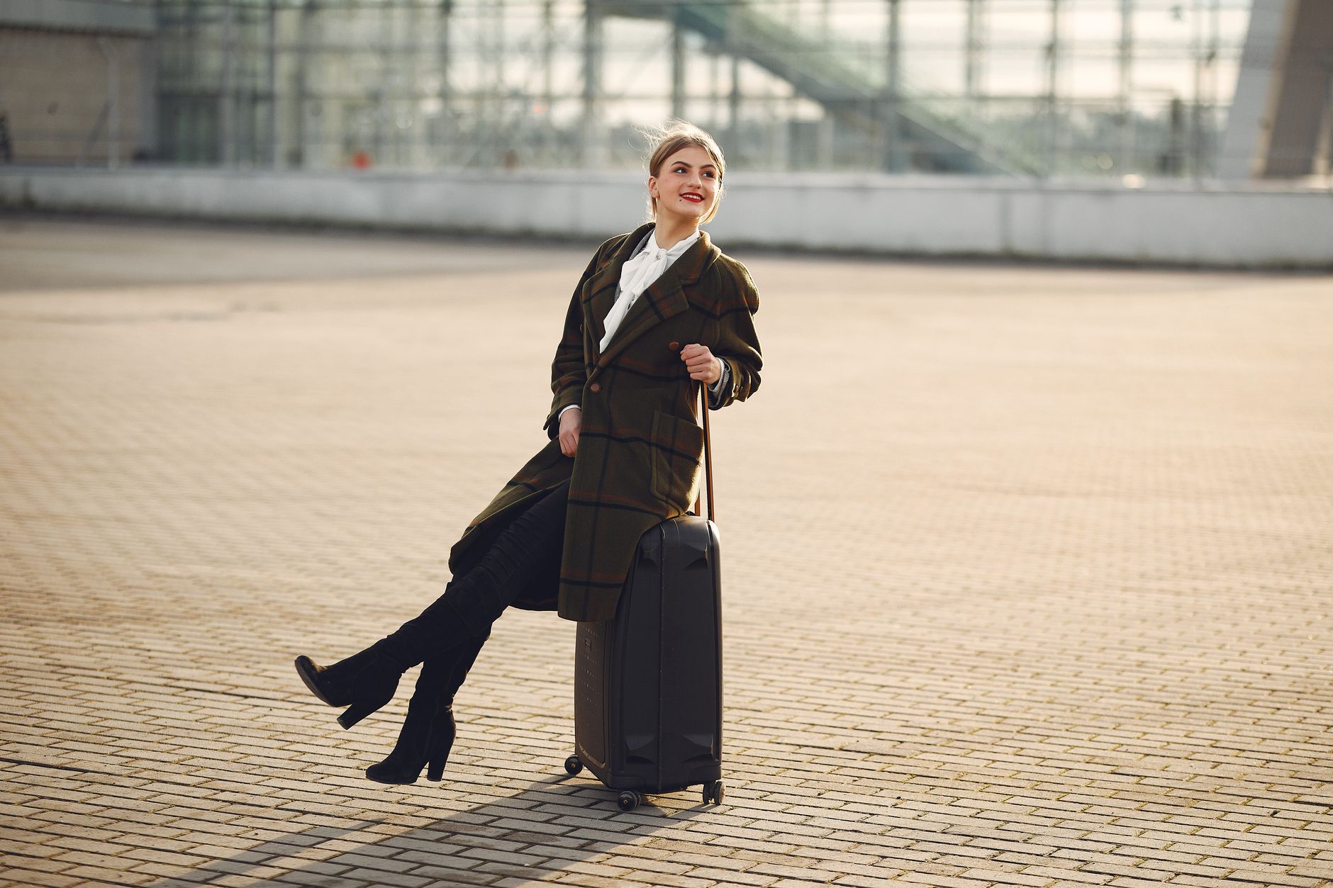 A stylish woman in a coat poses with her suitcase at Istanbul airport, symbols of solo travel.