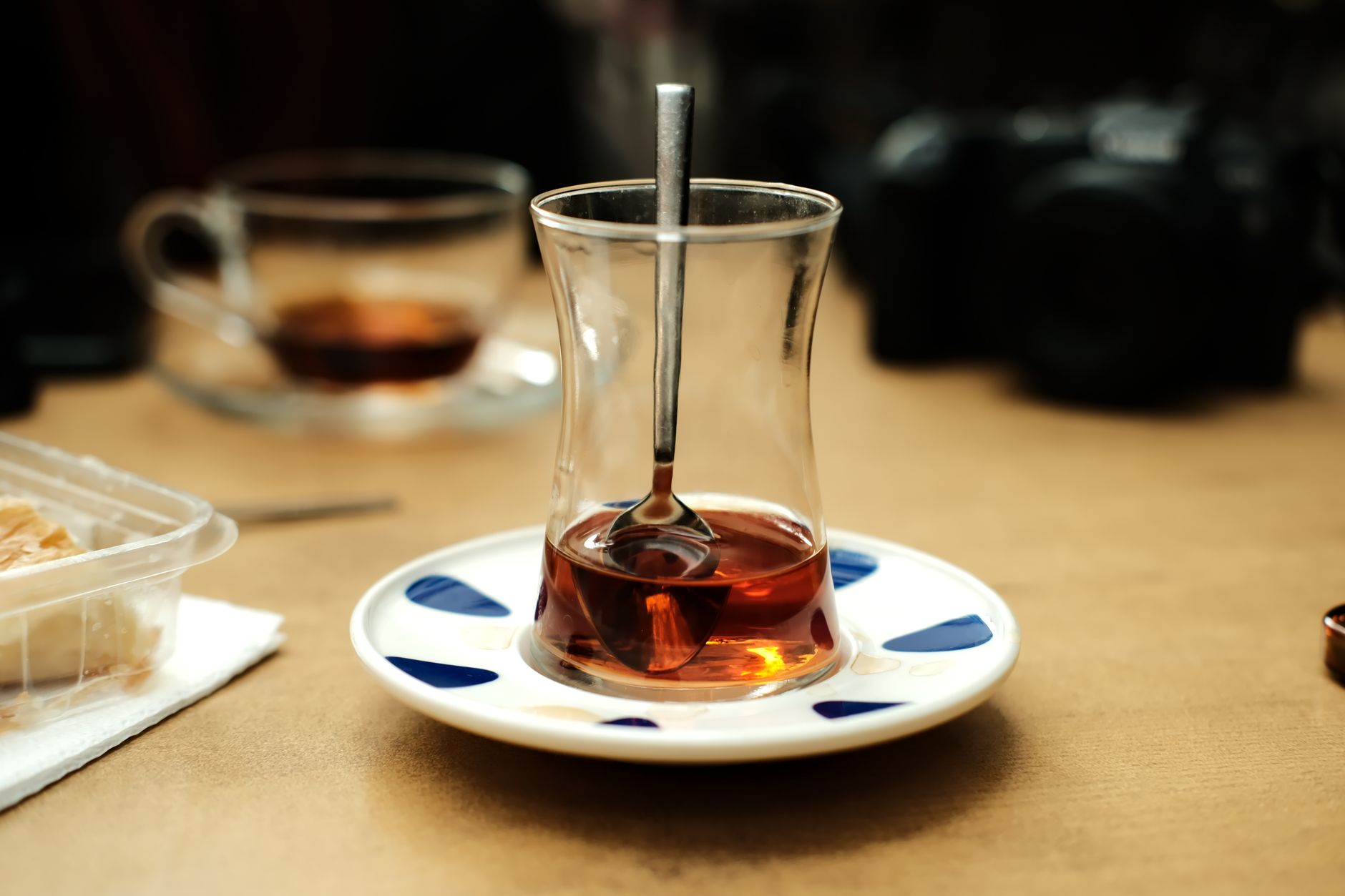 A glass of Turkish tea with a spoon, accompanied by Turkish delight on a plate.