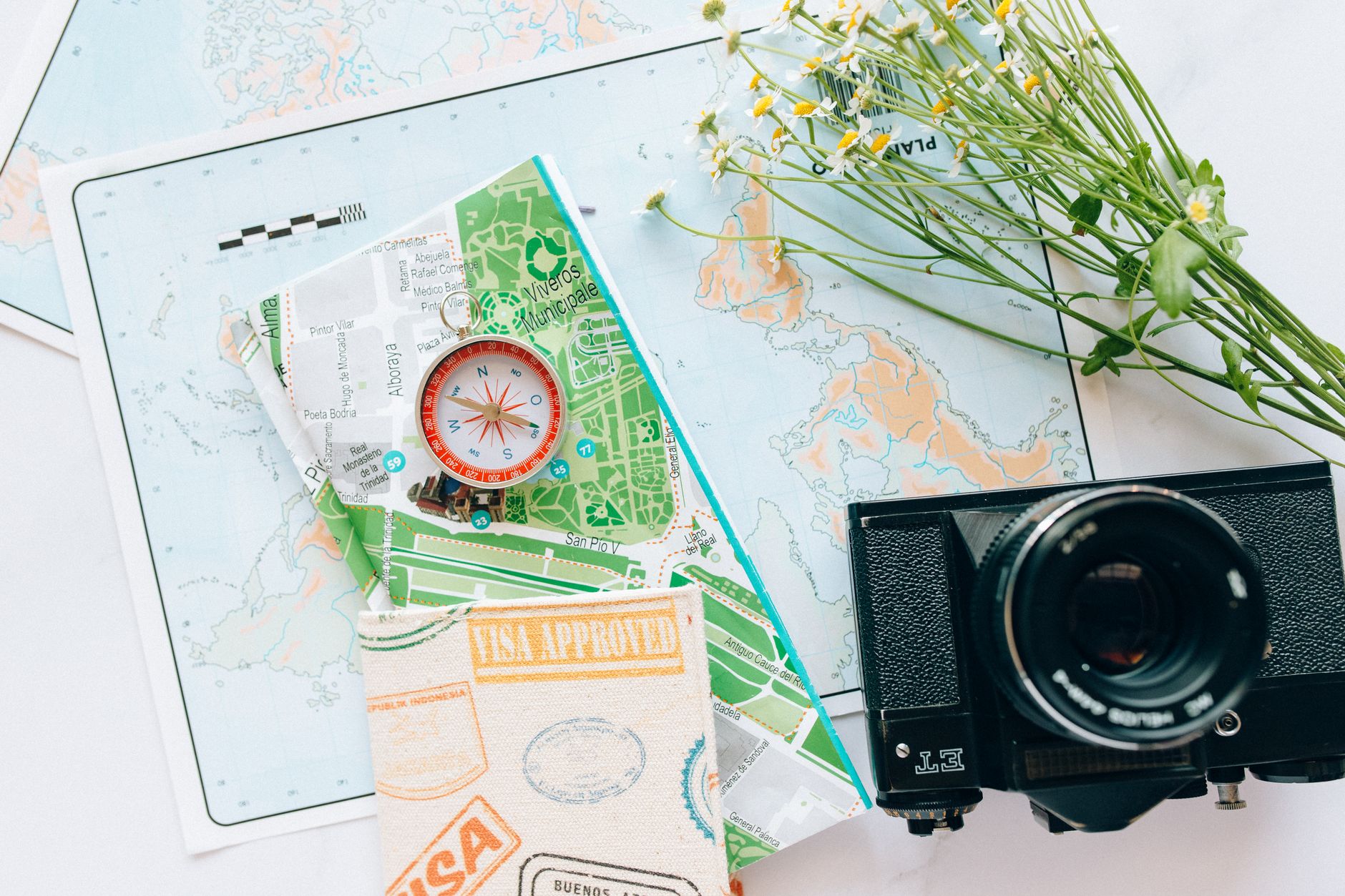 Close-up of travel gear including maps, a compass, a camera, and flowers.