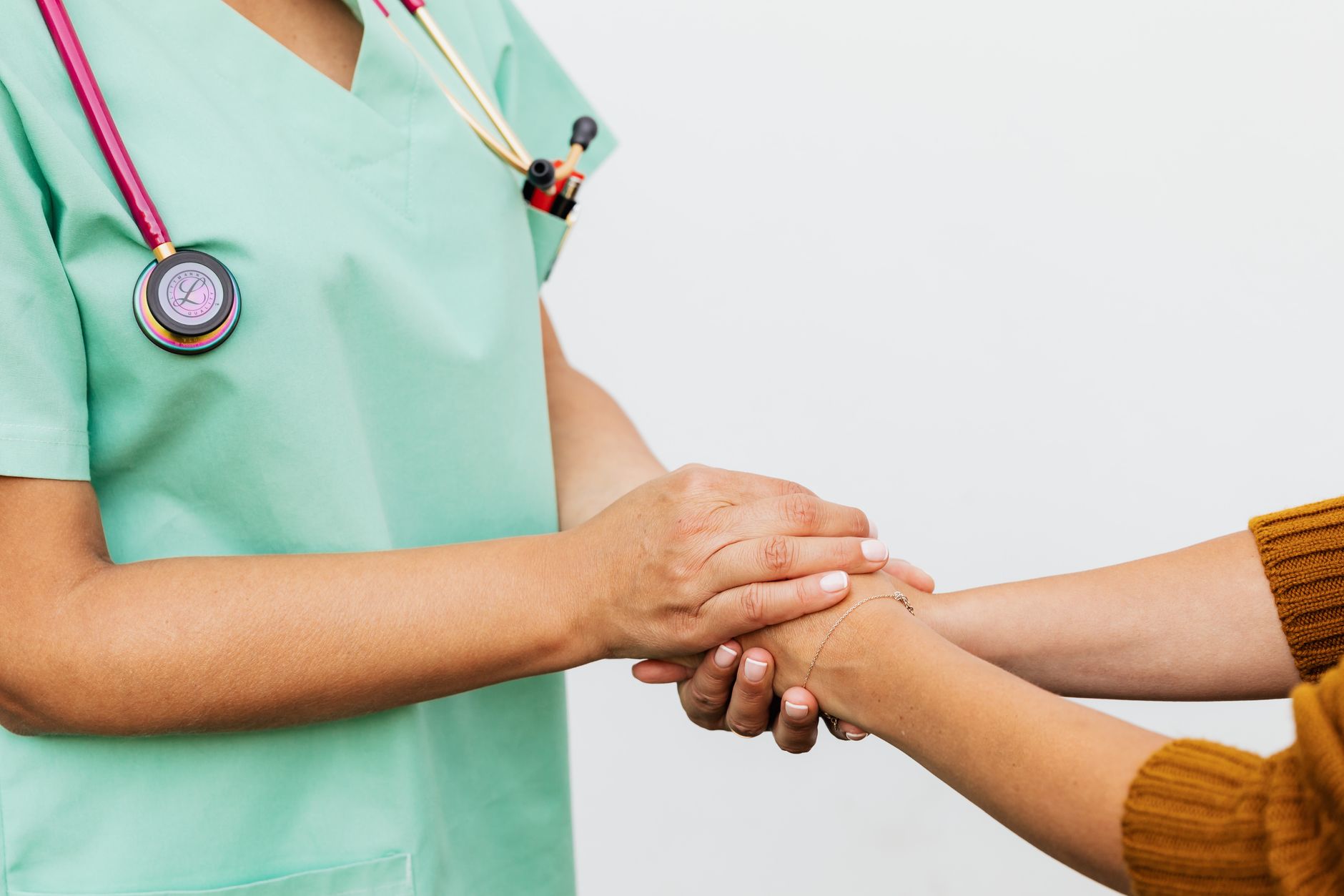 A nurse in scrubs gently holds the hands of a cancer patient, offering support.