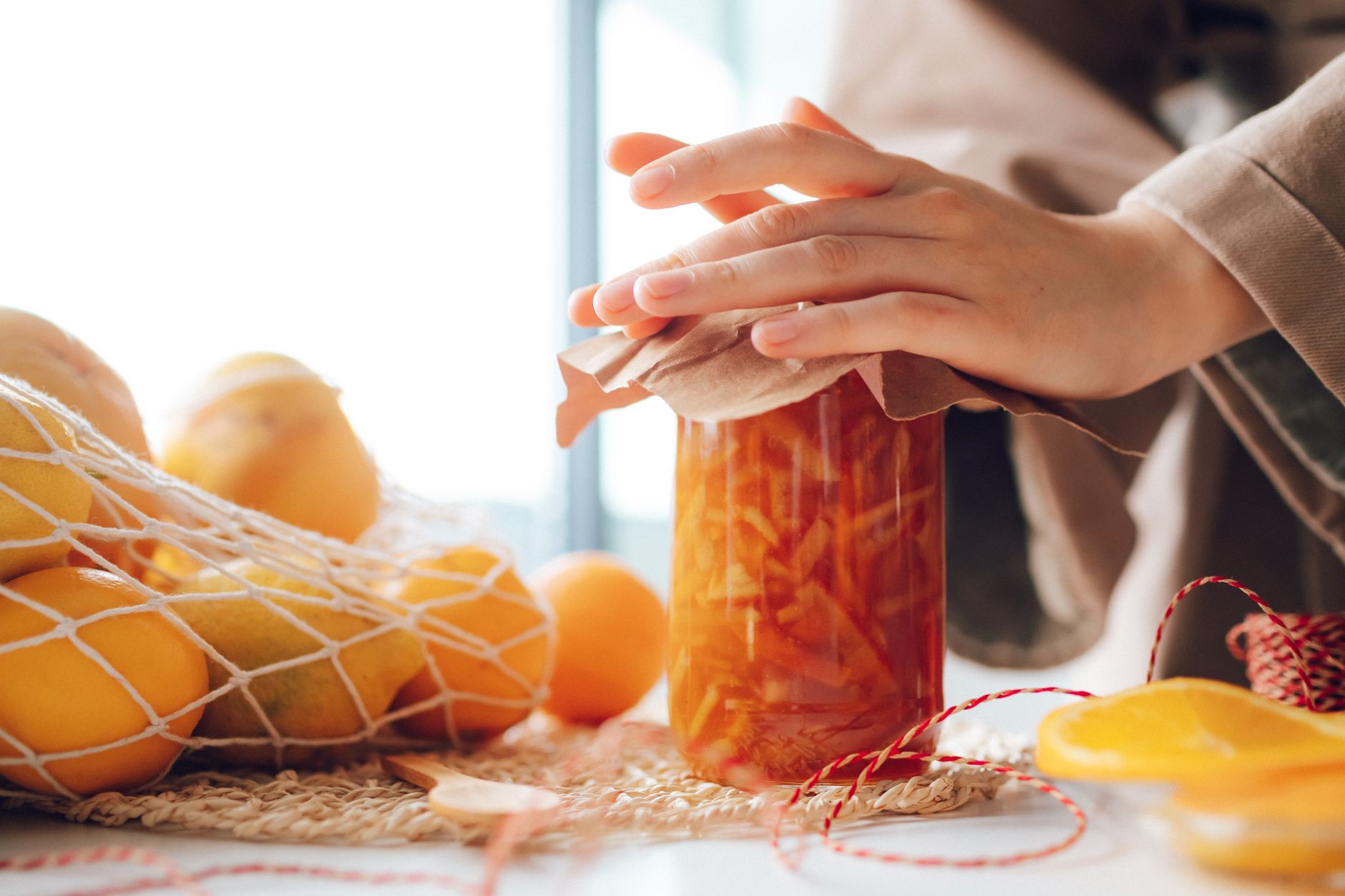 Close-up of hands sealing a jar of homemade citrus jam with lemons in the background.