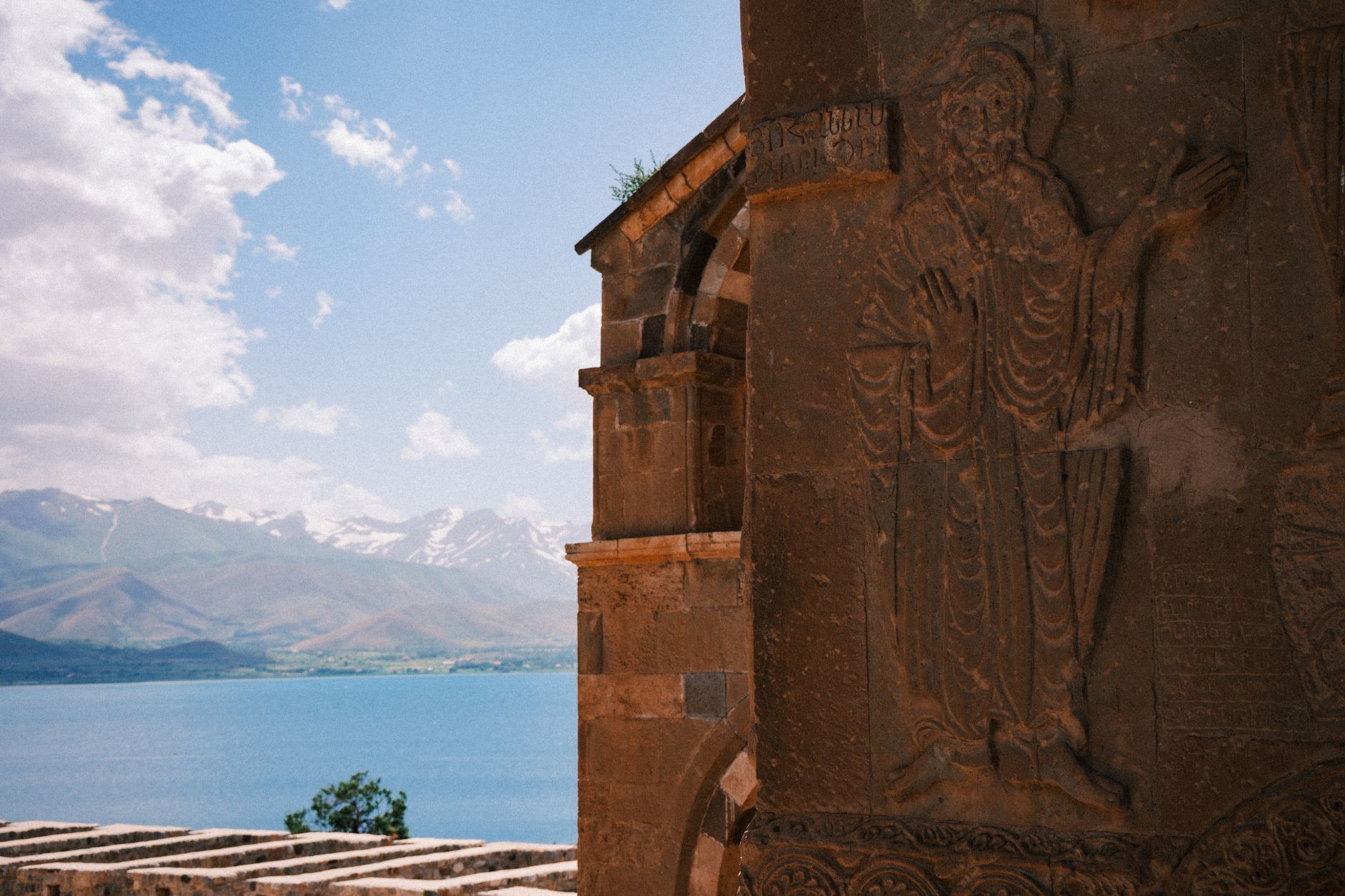 Arka planda Van Gölü ve dağlarla birlikte kilise duvarındaki oyma figür.
