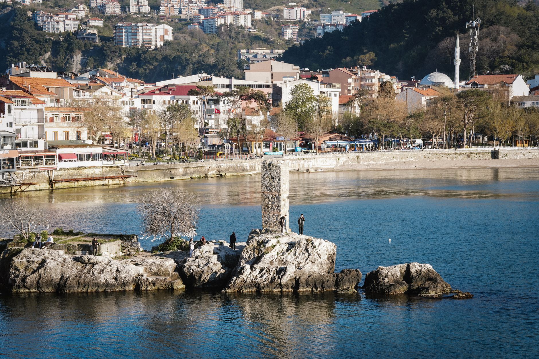 Taş bir yapı, kayalık çıkıntı ve çevredeki binalarla Amasra kıyı manzarası.