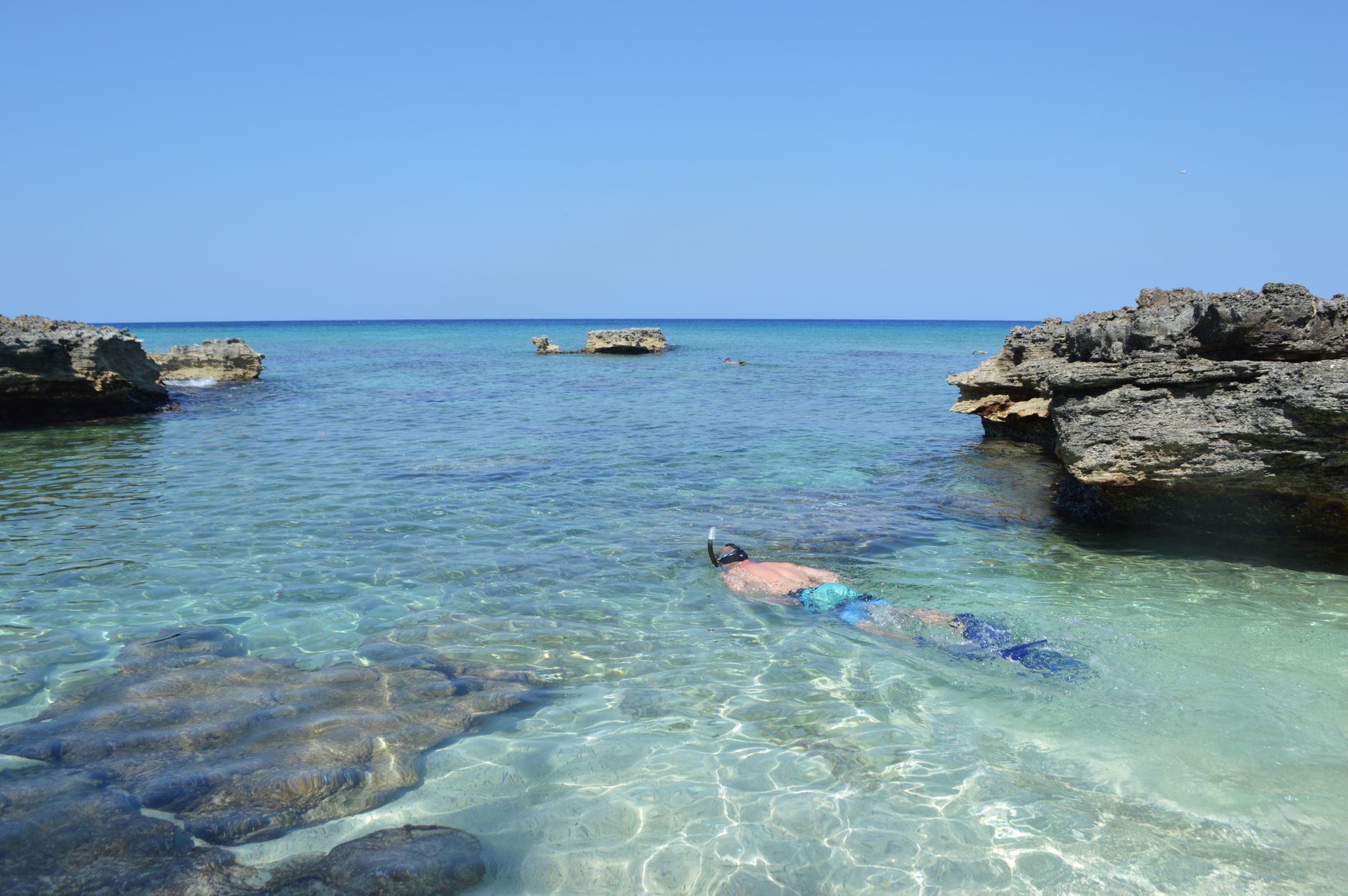 A beginner snorkeler floats in clear water over ancient ruins on the Lycian coast, surrounded by rocky seabed.