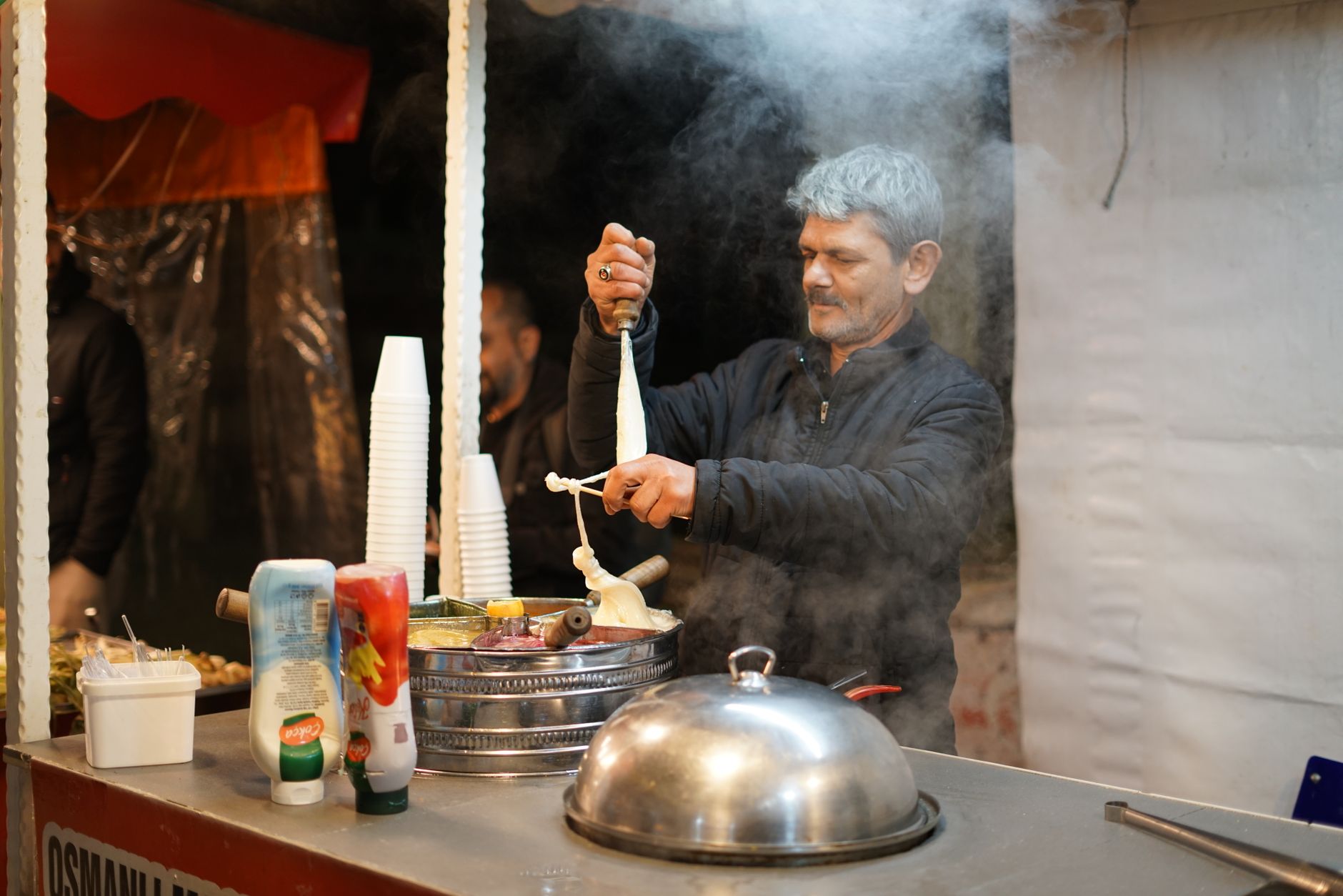 یک فروشنده در یک مغازه اصیل دوندرما در قهرمان‌مراش در میان بخار بستنی سنتی آماده می‌کند.