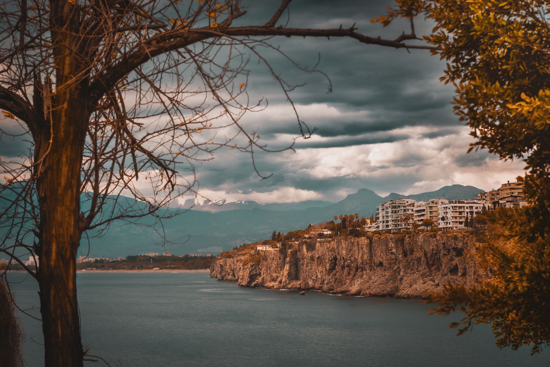 View of Antalya's coastline in autumn, featuring cliffs, a tranquil sea, and dramatic clouds.