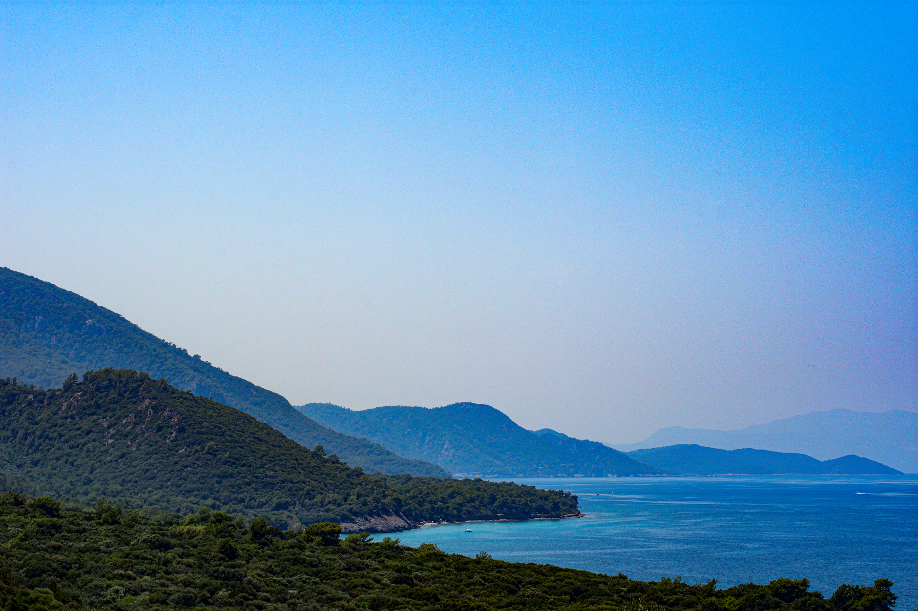 爱琴海海岸的宁静景色，郁郁葱葱的绿色山丘和清澈湛蓝的海水。