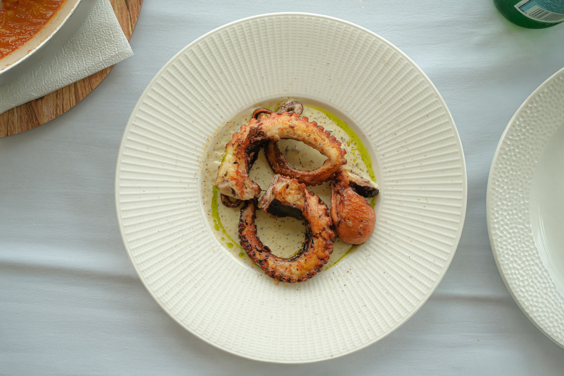 Delicious grilled octopus served on a white plate, garnished with olive oil.