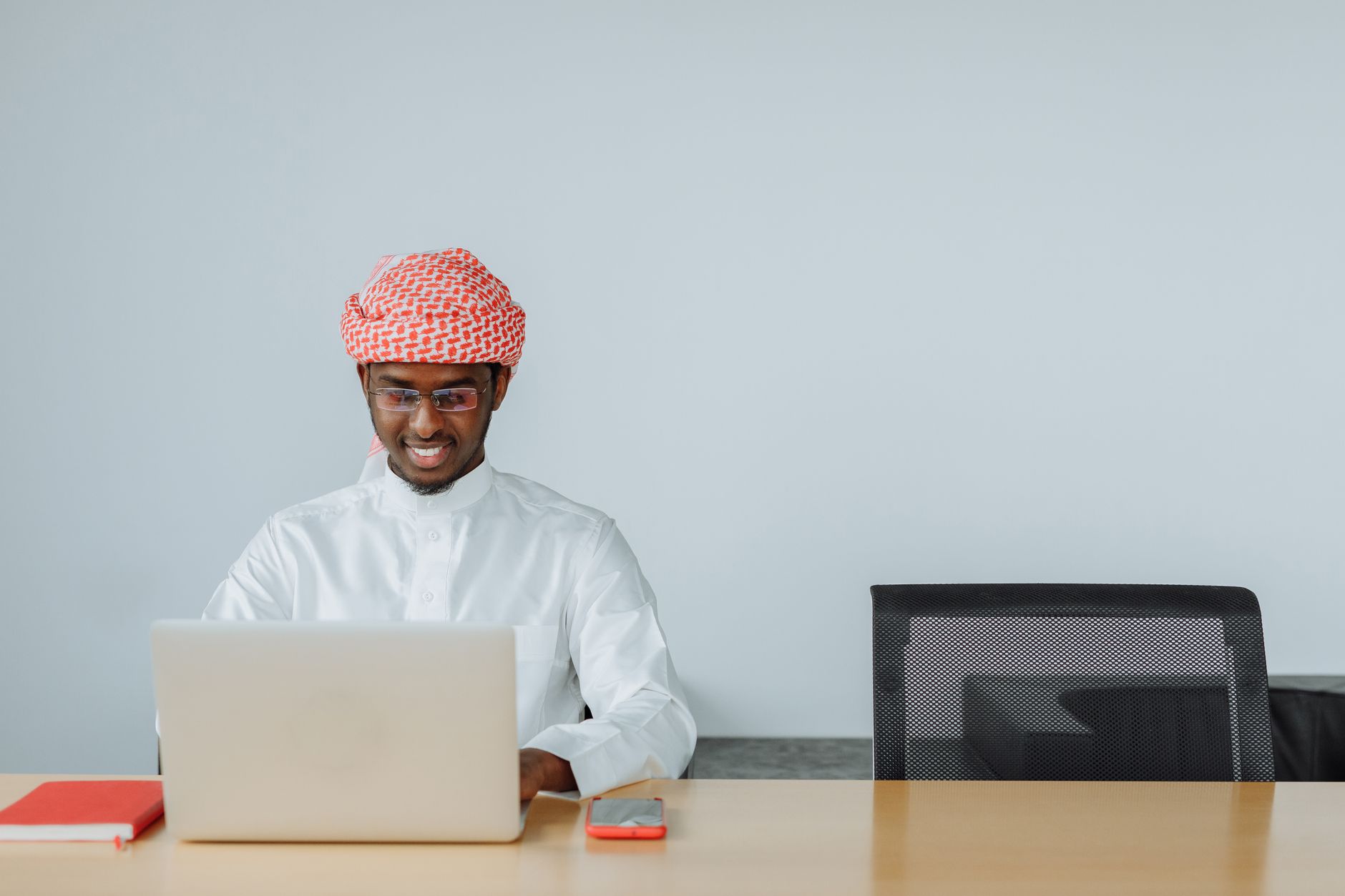 Gulf region man in traditional attire on a laptop for a remote consultation.