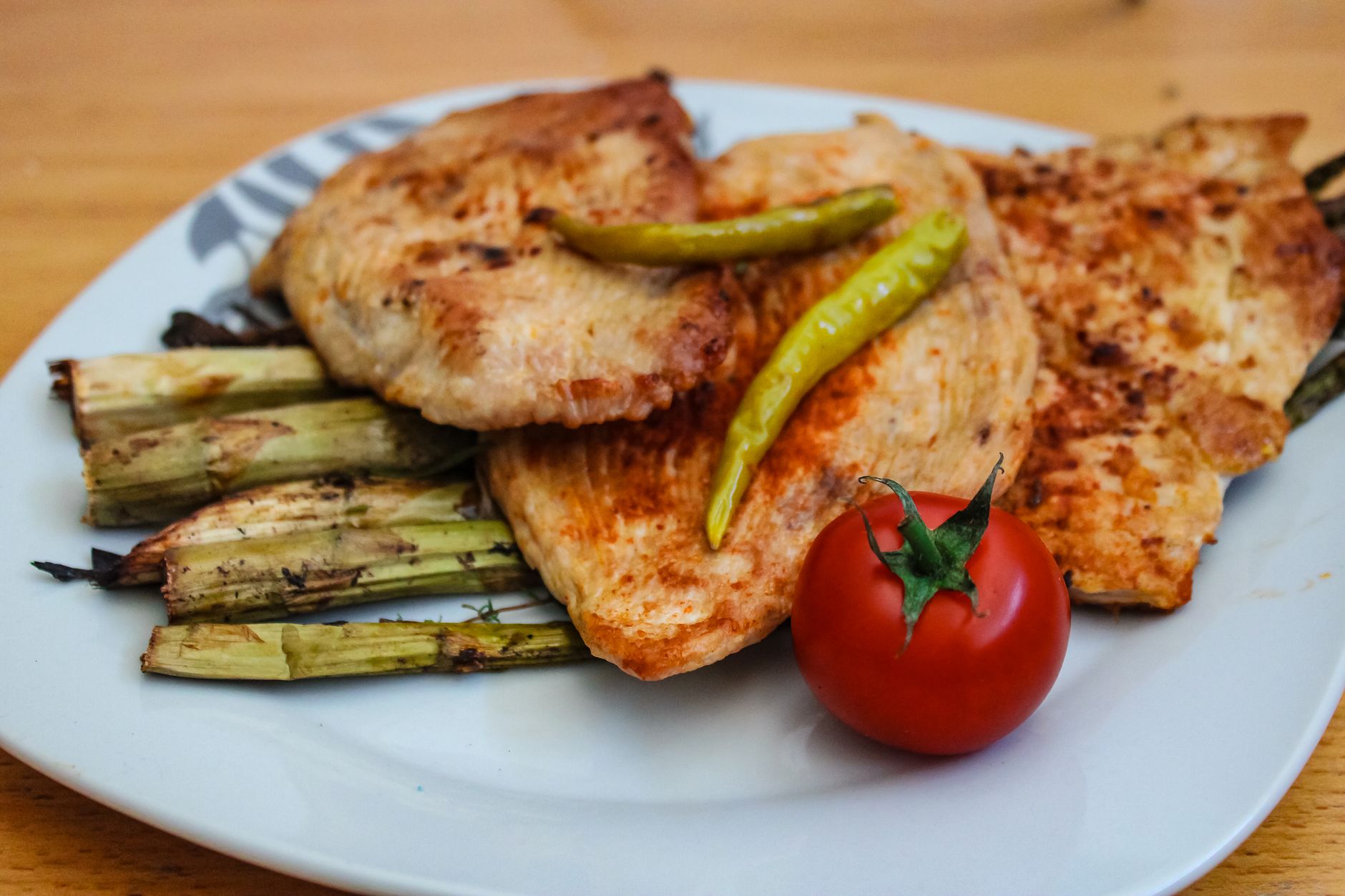Plated meal featuring grilled fish, green peppers, and fresh tomato, showcasing a Turkish culinary style.