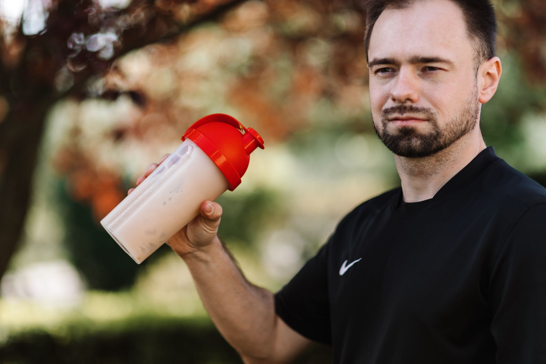 A man in a black shirt holds a protein shake outdoors, preparing for a pre-operative diet.