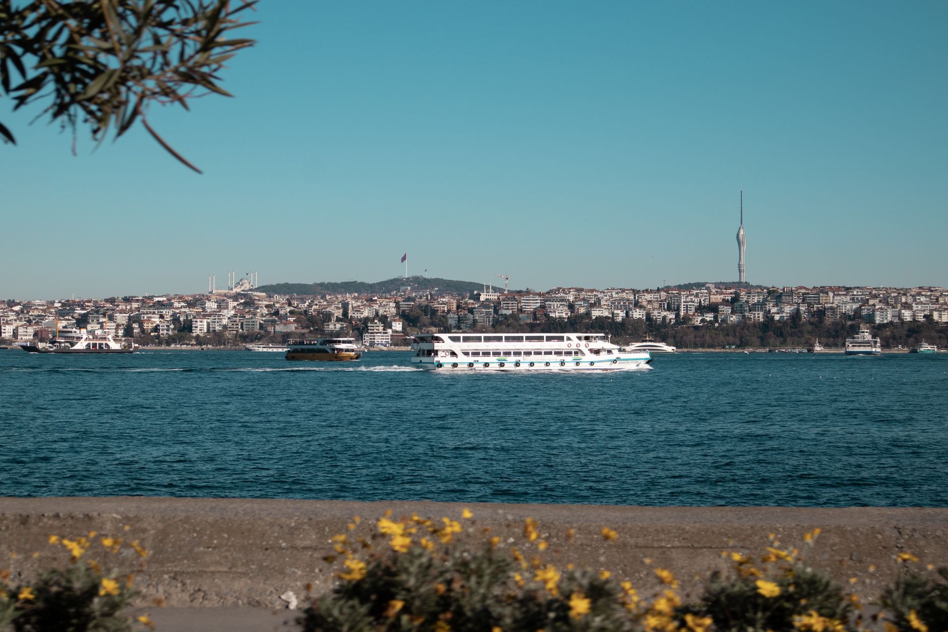 A scenic view of the Istanbul waterfront featuring boats on the water and a tall tower in the background.