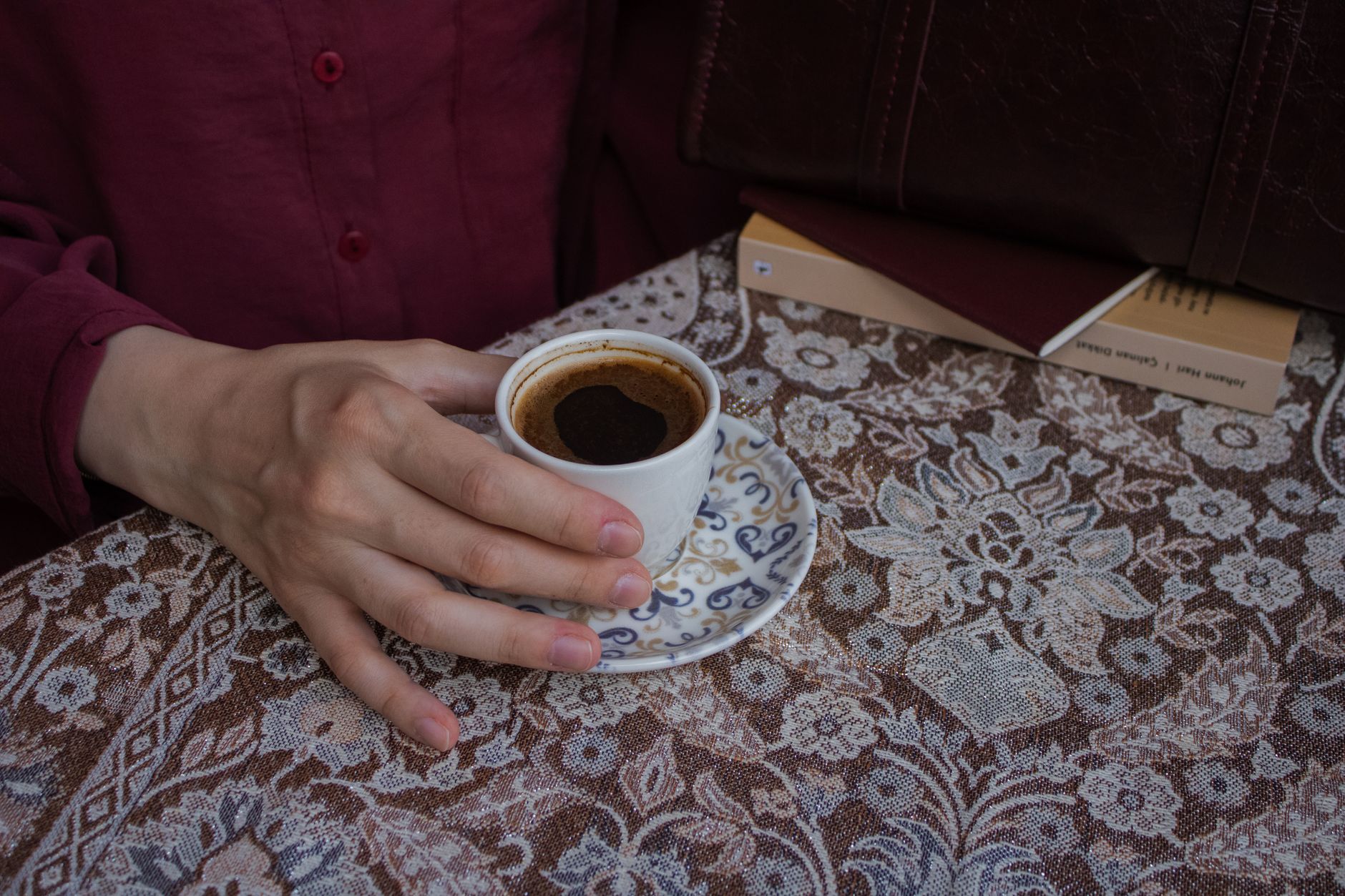 دستی فنجان قهوه ترک را روی رومیزی تزئینی در یک کافه نگه داشته است.