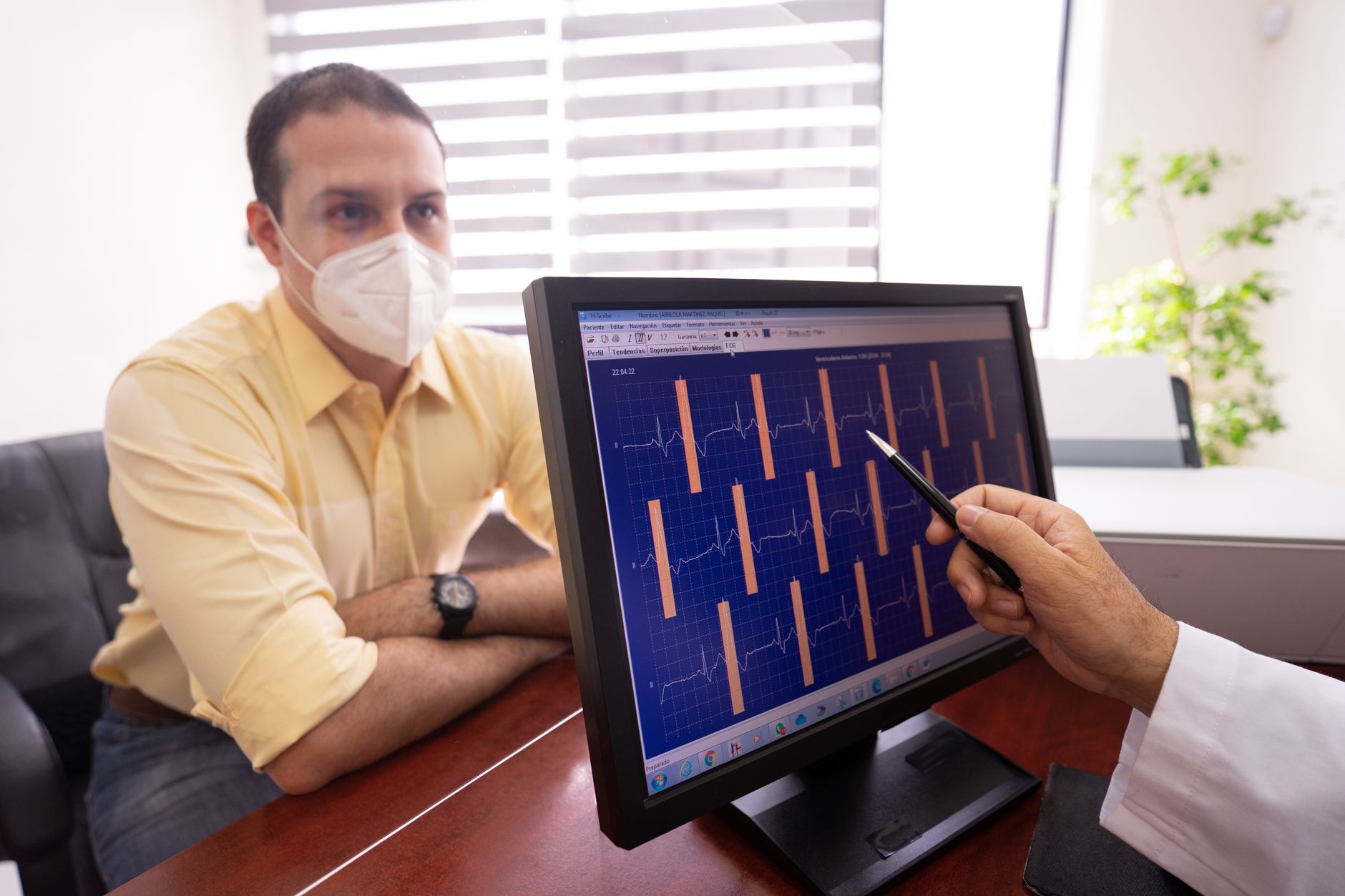 A cardiologist shows cardiac CT images on a monitor to a patient wearing a mask.