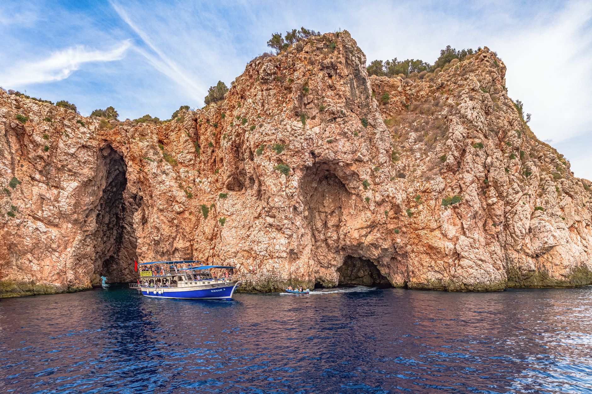 Boat near the rocky entrance of Karain Cave, showcasing limestone formations and blue waters in Antalya.