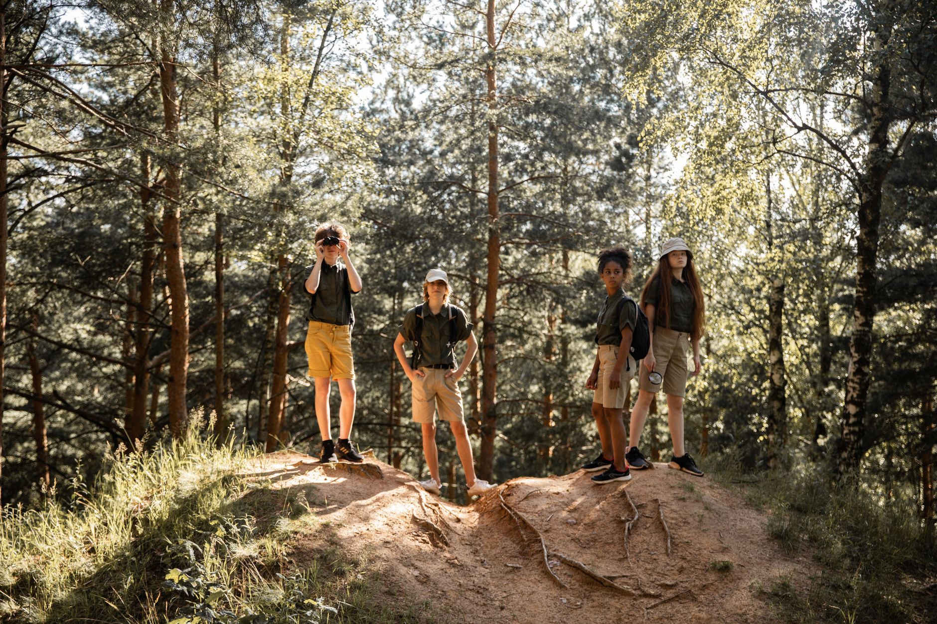 A group of children in a forest, one using a camera, all dressed in outdoor gear.