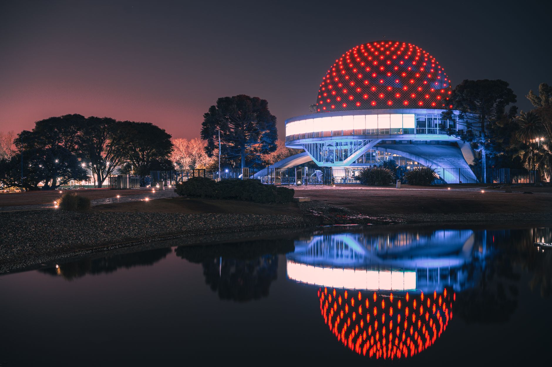 A family enjoying a planetarium dome show, with vibrant lights reflected in a calm water surface.