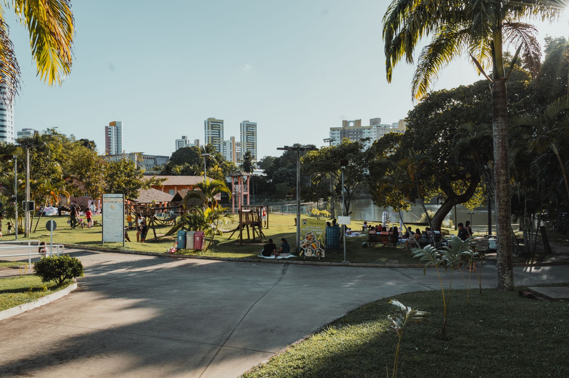 Families picnicking and playing in Ankara park, with playgrounds and skyscrapers in the background.