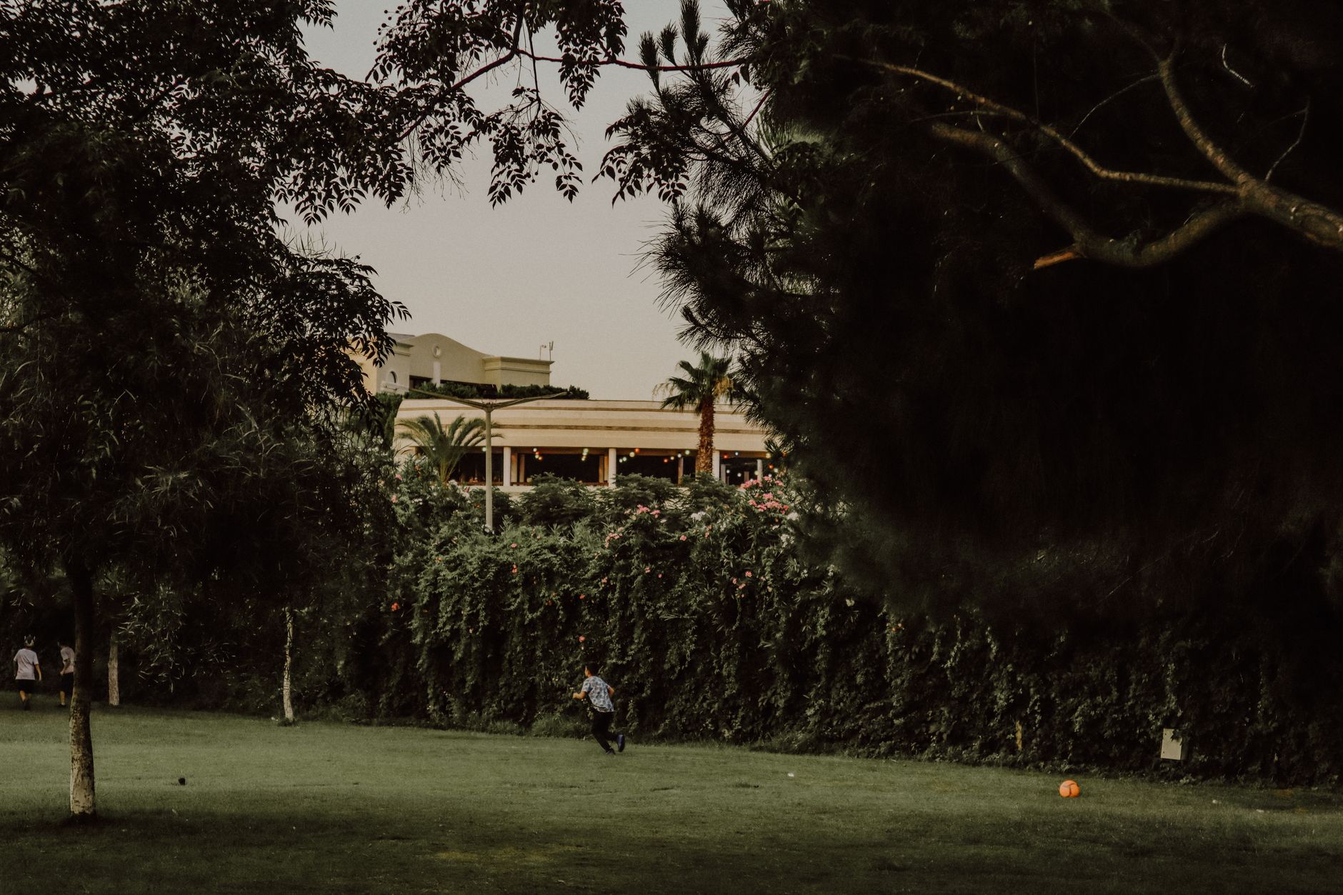 A view of shaded lawns in Kültürpark, Izmir, with a child playing and lush greenery.