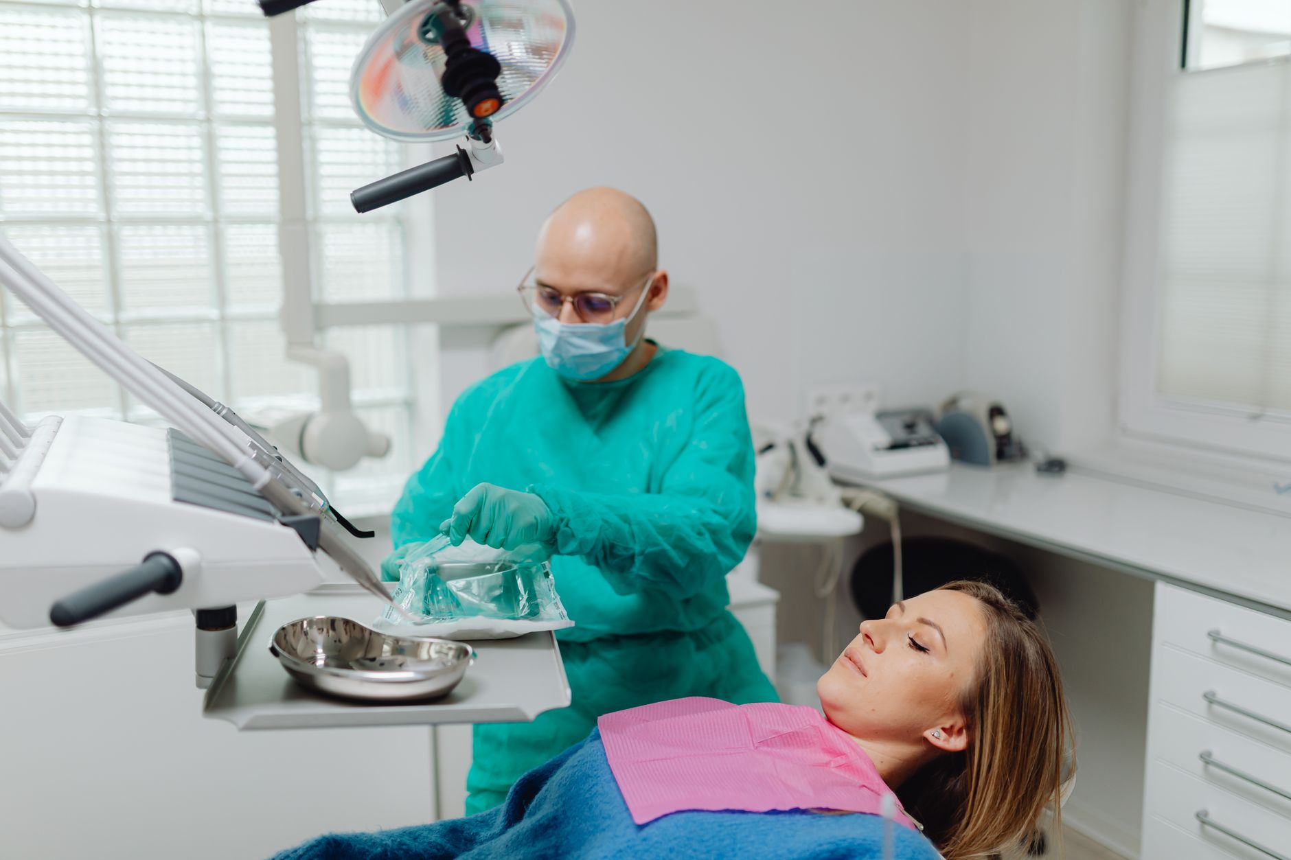 A dentist in green attire preparing for a procedure while a patient relaxes in a dental chair.