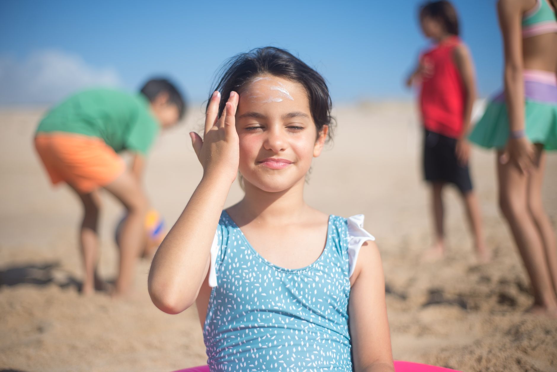 A child applying sunscreen on her face at the beach, promoting sun safety.