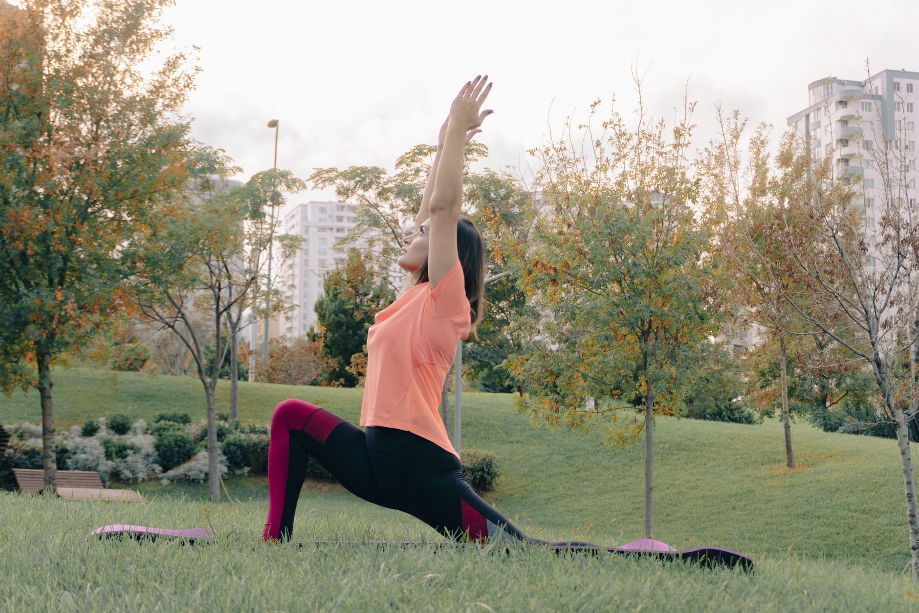 A woman practicing yoga outdoors in a park, stretching with arms raised.