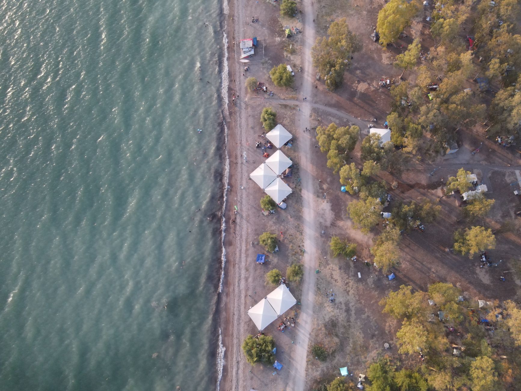 Aerial view of campers in hammocks and tents among olive trees near the sea in Datça.