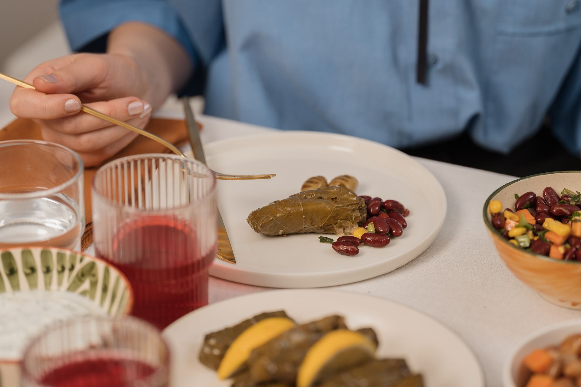 A hand holds a fork over a plate with vine leaves and beans, part of a healthy meal.