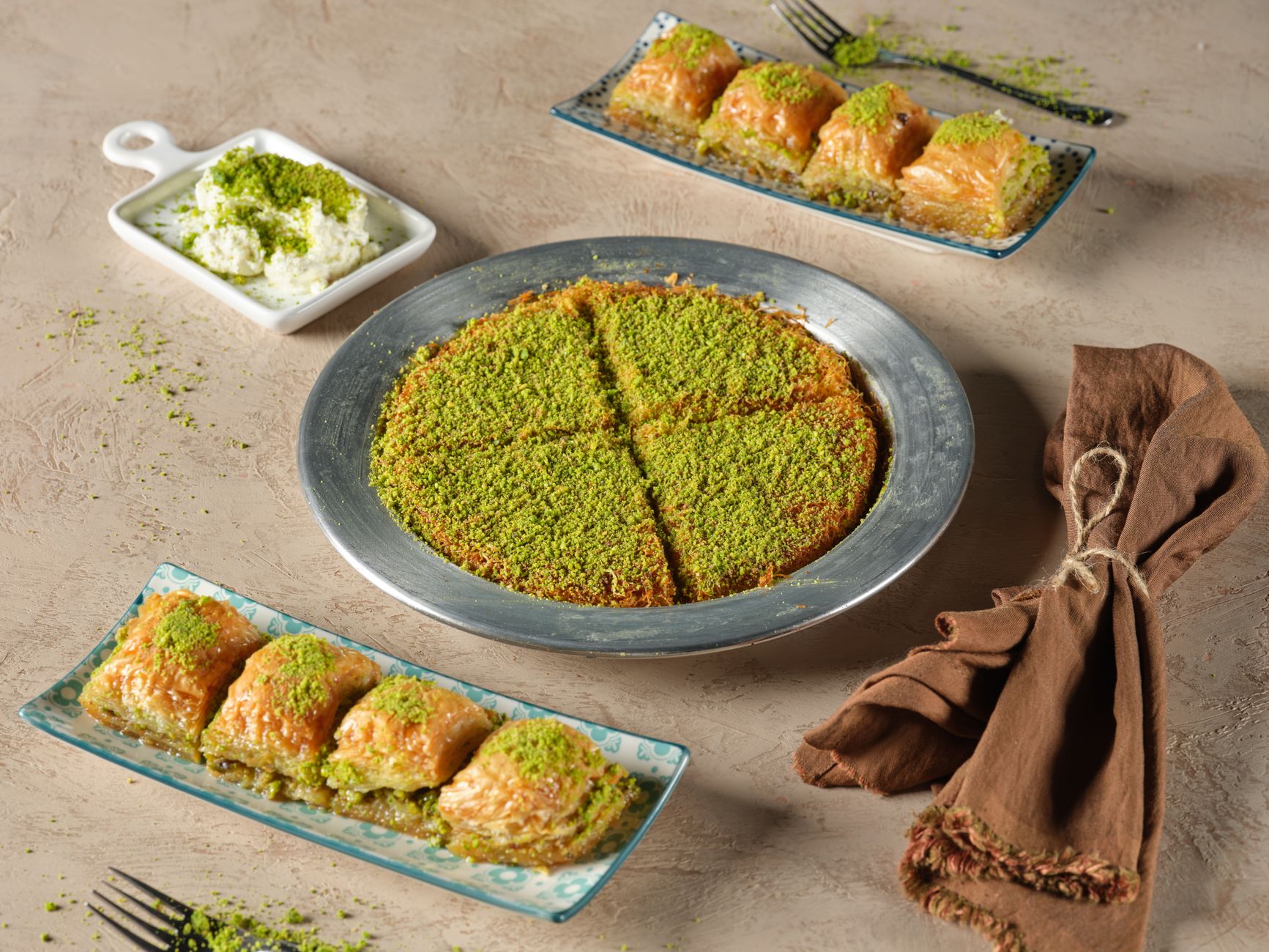 نمای نزدیک باklava و کونفه با پستهٔ سبز روی سینی نقره‌ای.