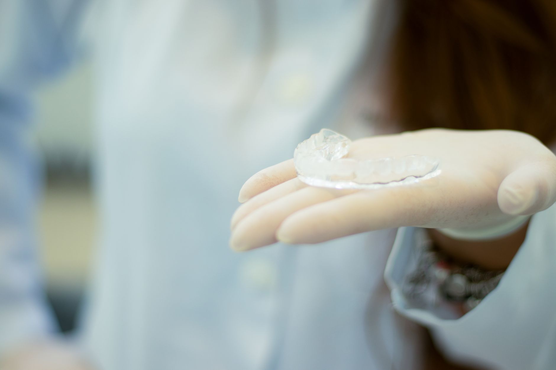A dentist holding a clear custom occlusal splint on their gloved hand.