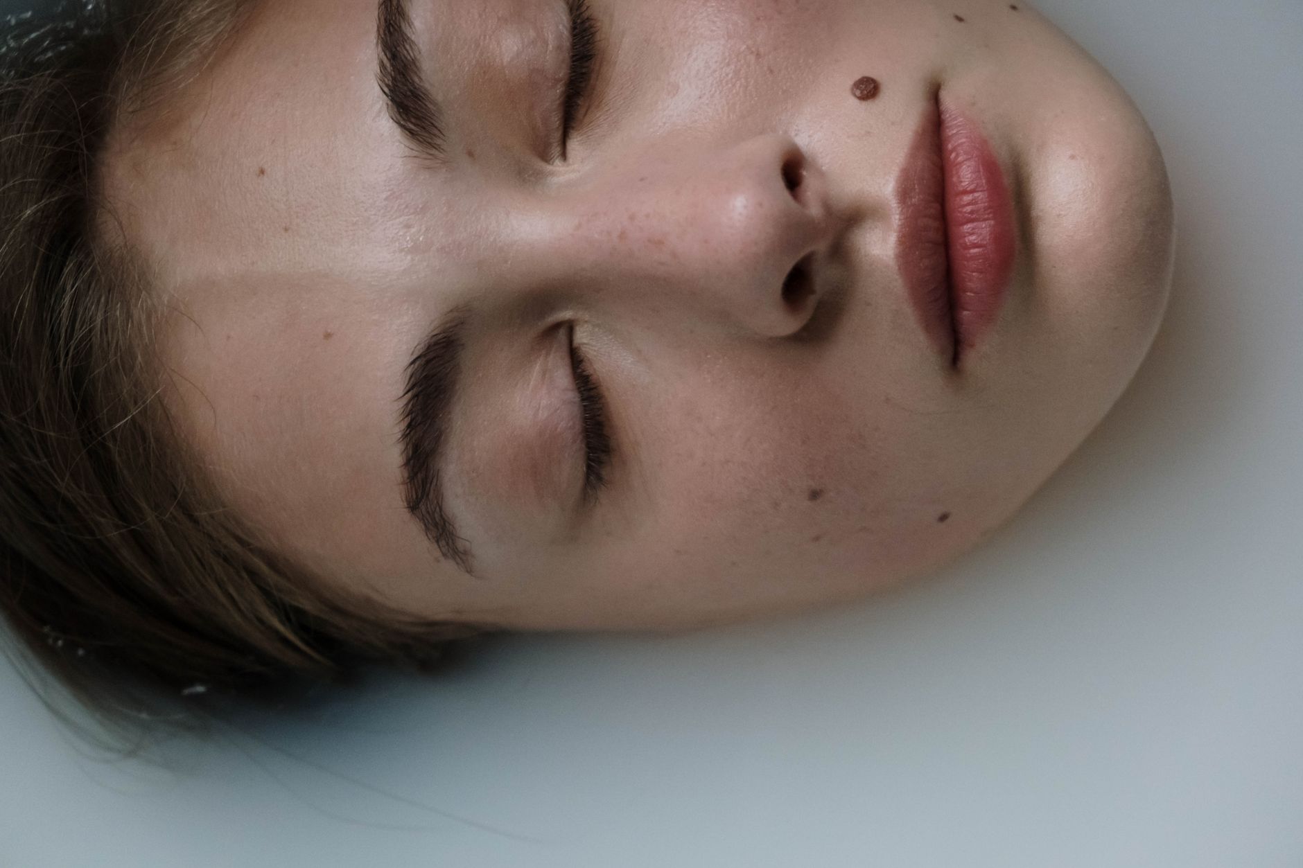 Close-up image of a person's face submerged in milky water.