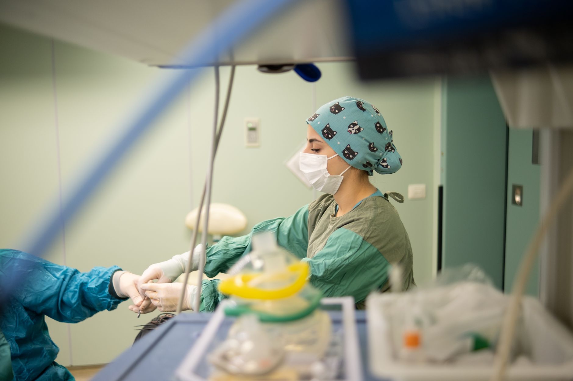 A nurse in a patterned surgical cap monitors a dialysis patient in a bright clinic.